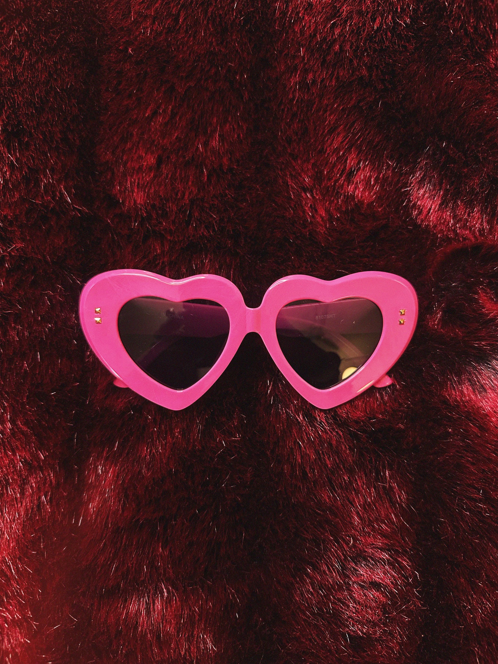 Pink heart-shaped sunglasses on a red furry surface