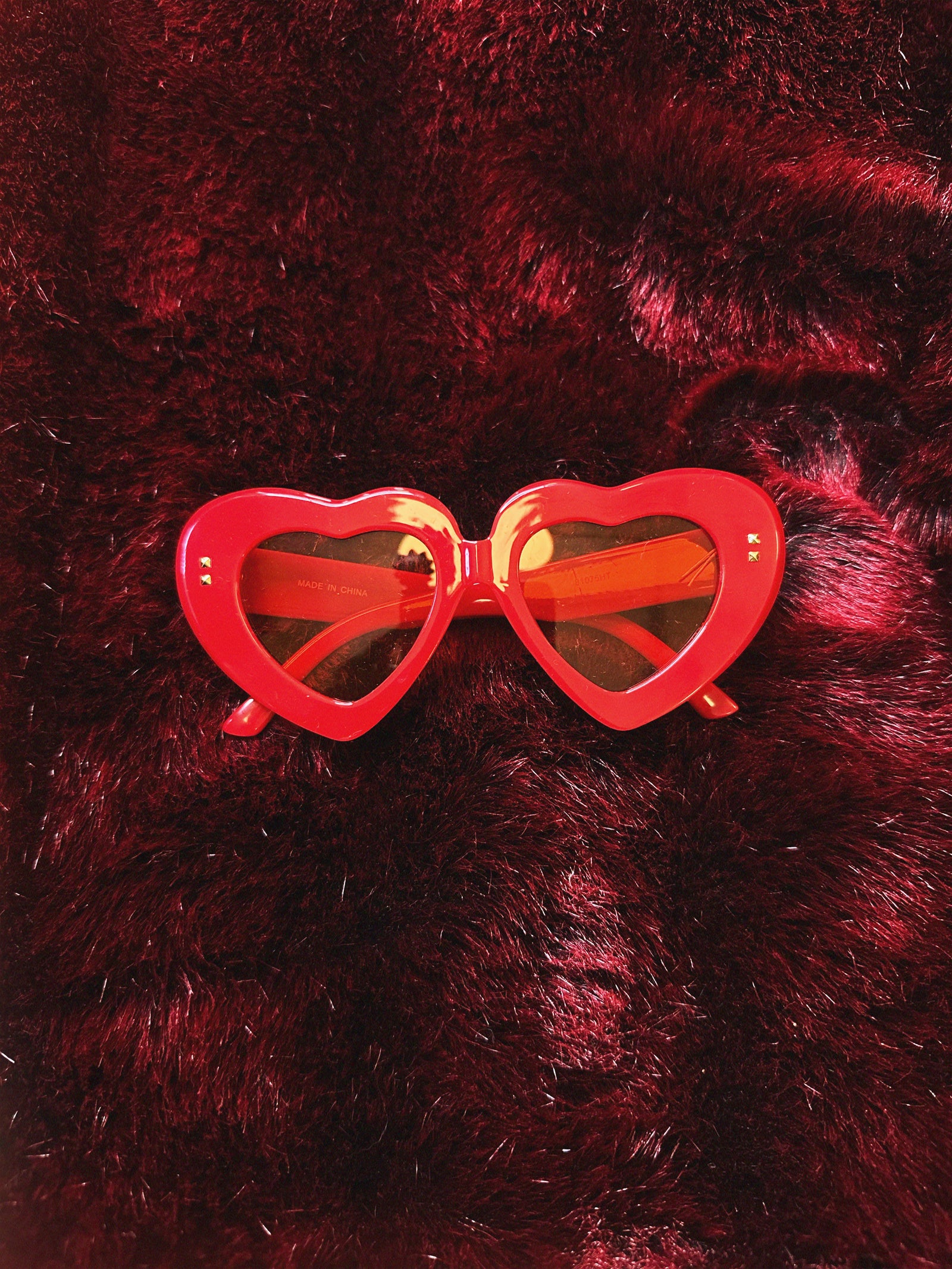 Red heart-shaped sunglasses on a dark red textured background