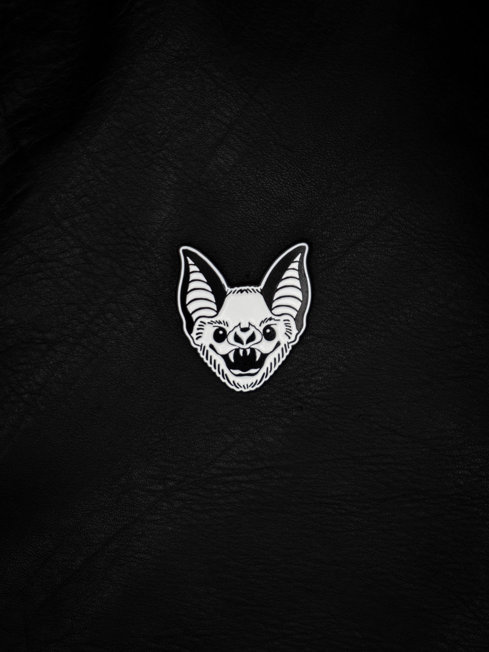 A black and white enamel pin with a bat design.