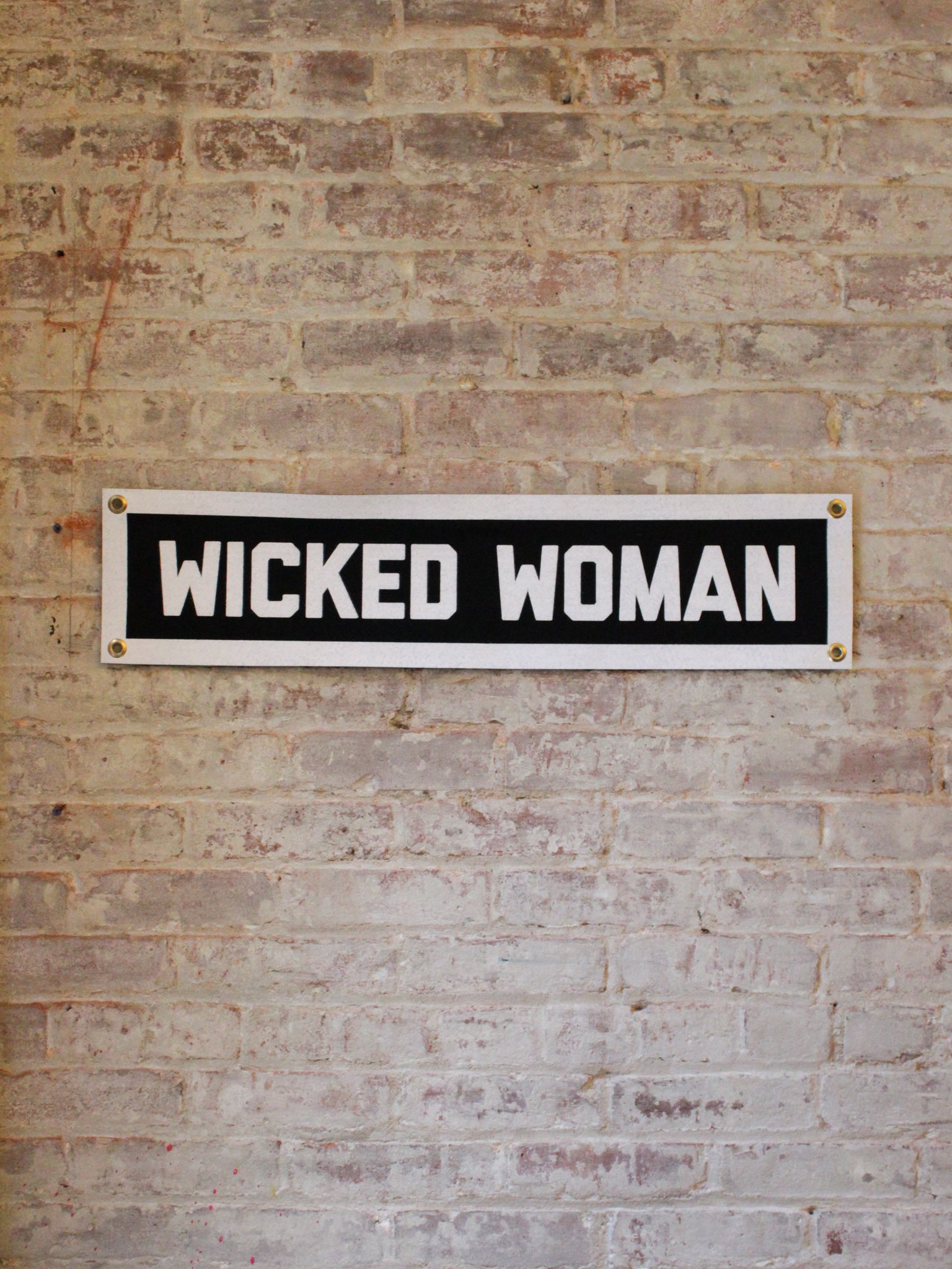 black and white rectangle banner with 4 gold grommets reads "wicked woman"