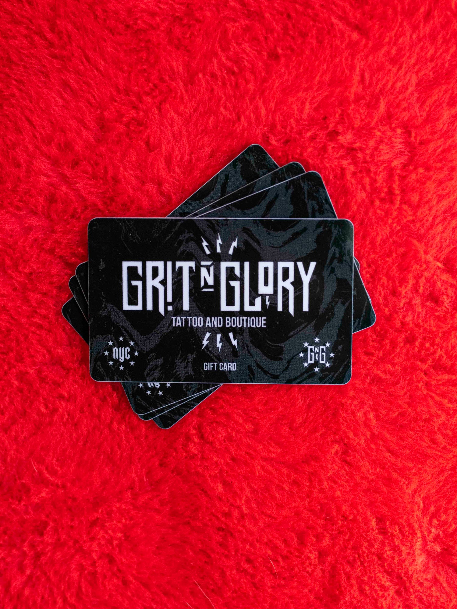 Stack of Grit N Glory gift cards on a fuzzy red background