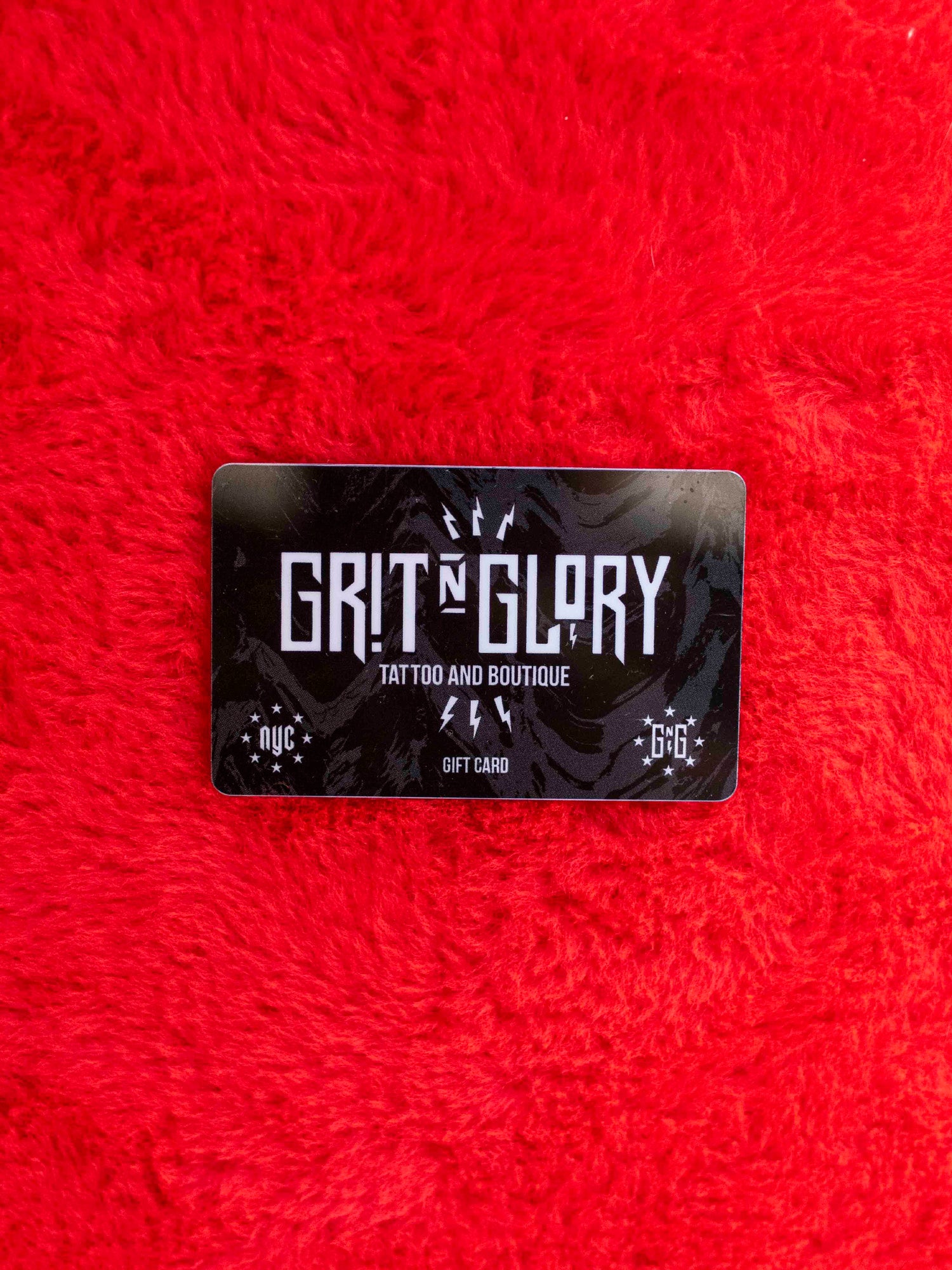 Grit N Glory gift card in black white and gray on a fuzzy red background.