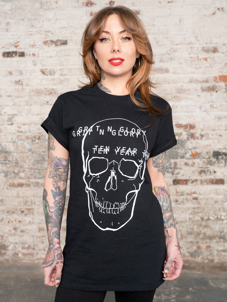 Megan Massacre wearing a unisex black t-shirt with a white skull and text in front of a brick wall.