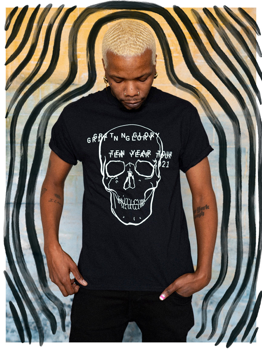 A person wearing a black graphic t-shirt with a white text and skull design on it, standing in front of a striped background.