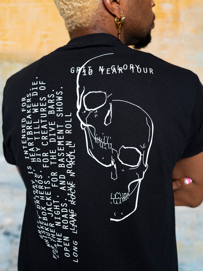 A person wearing a black graphic t-shirt with white text and split skull design on it. Text is across the top and down the back sideways.