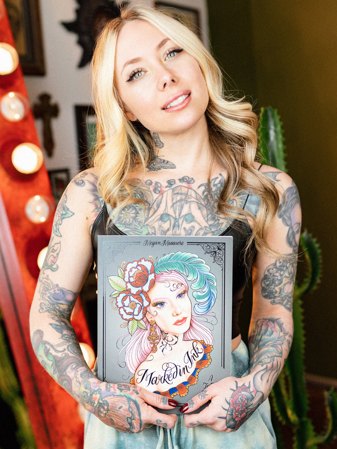 Megan Massacre holding her coloring book Marked In Ink. Coloring book cover features a drawing by Megan Massacre of a tattooed woman on a gray background.