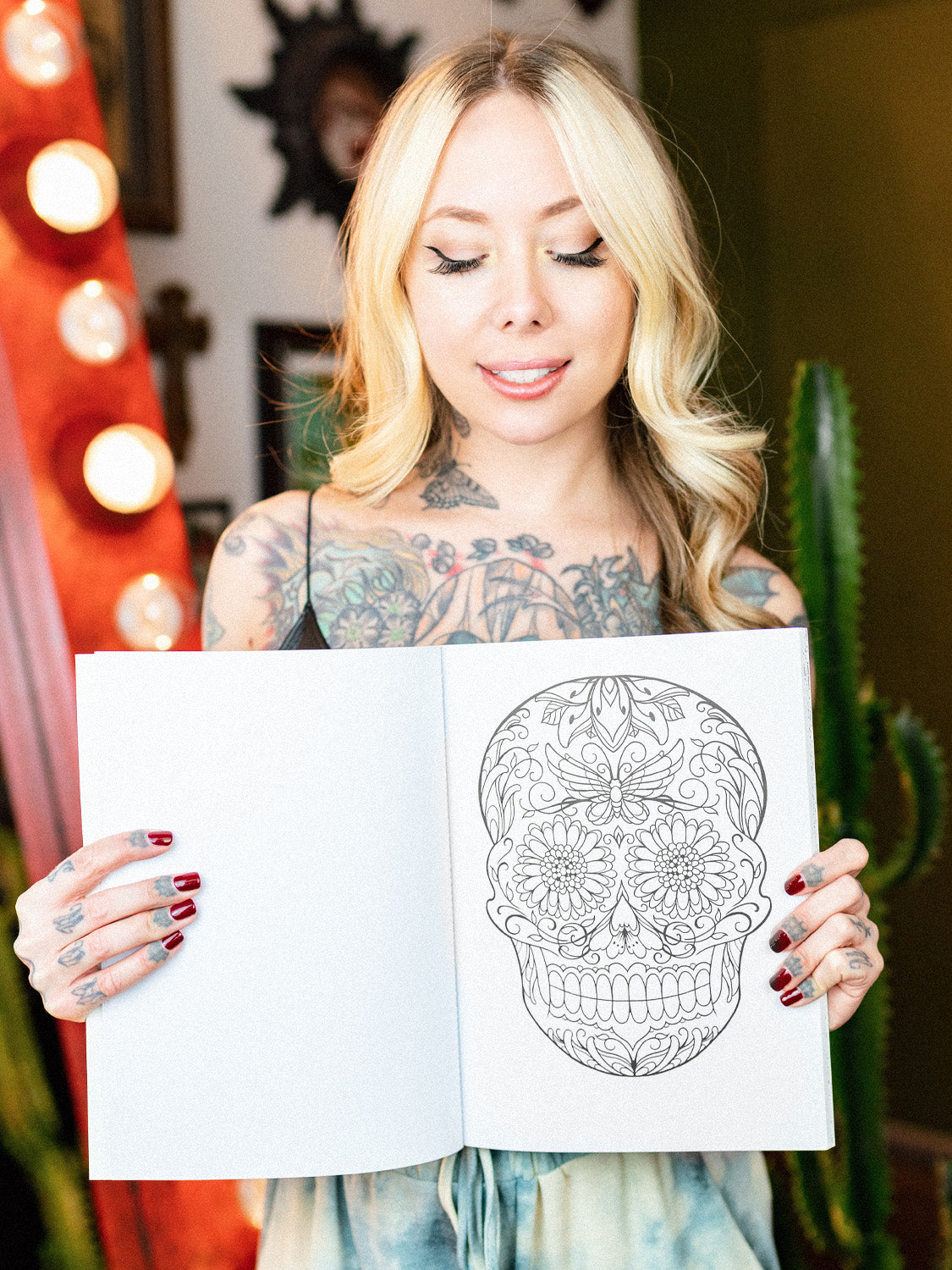 Megan Massacre holding her coloring book Marked in Ink open to an uncolored coloring page featuring a sugar skull with butterfly detail.