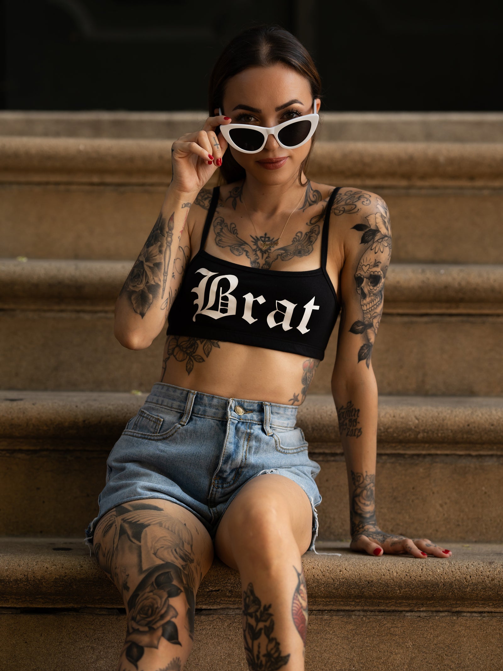 Janice Danger wearing the Brat black bralette with white sunglasses and blue denim shorts. 