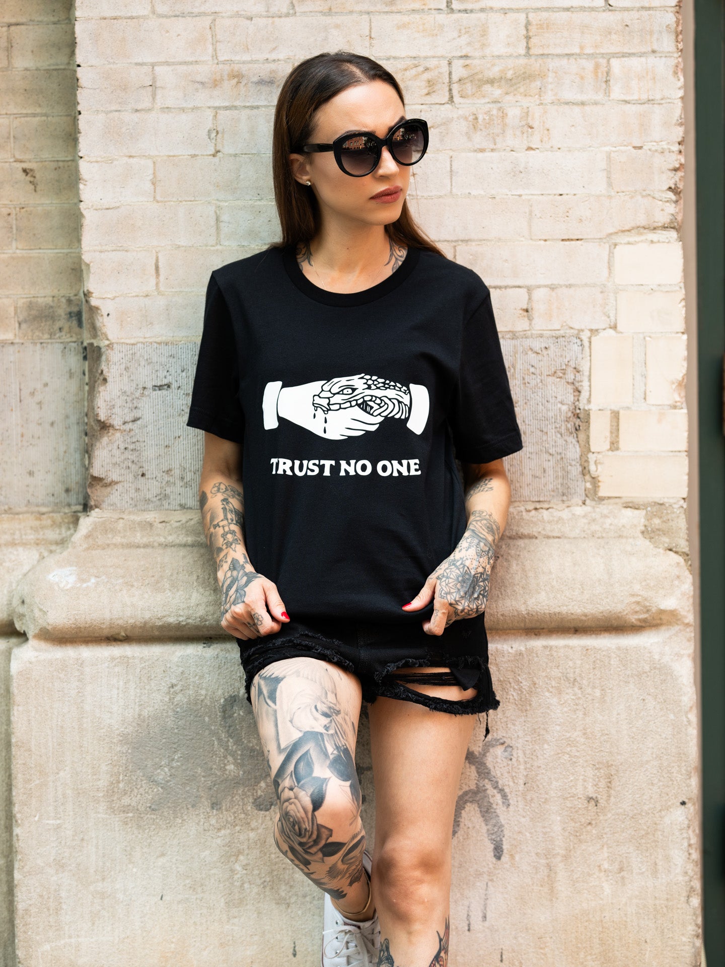 Janice Danger wearing a unisex black t-shirt that reads "trust no one" with denim shorts