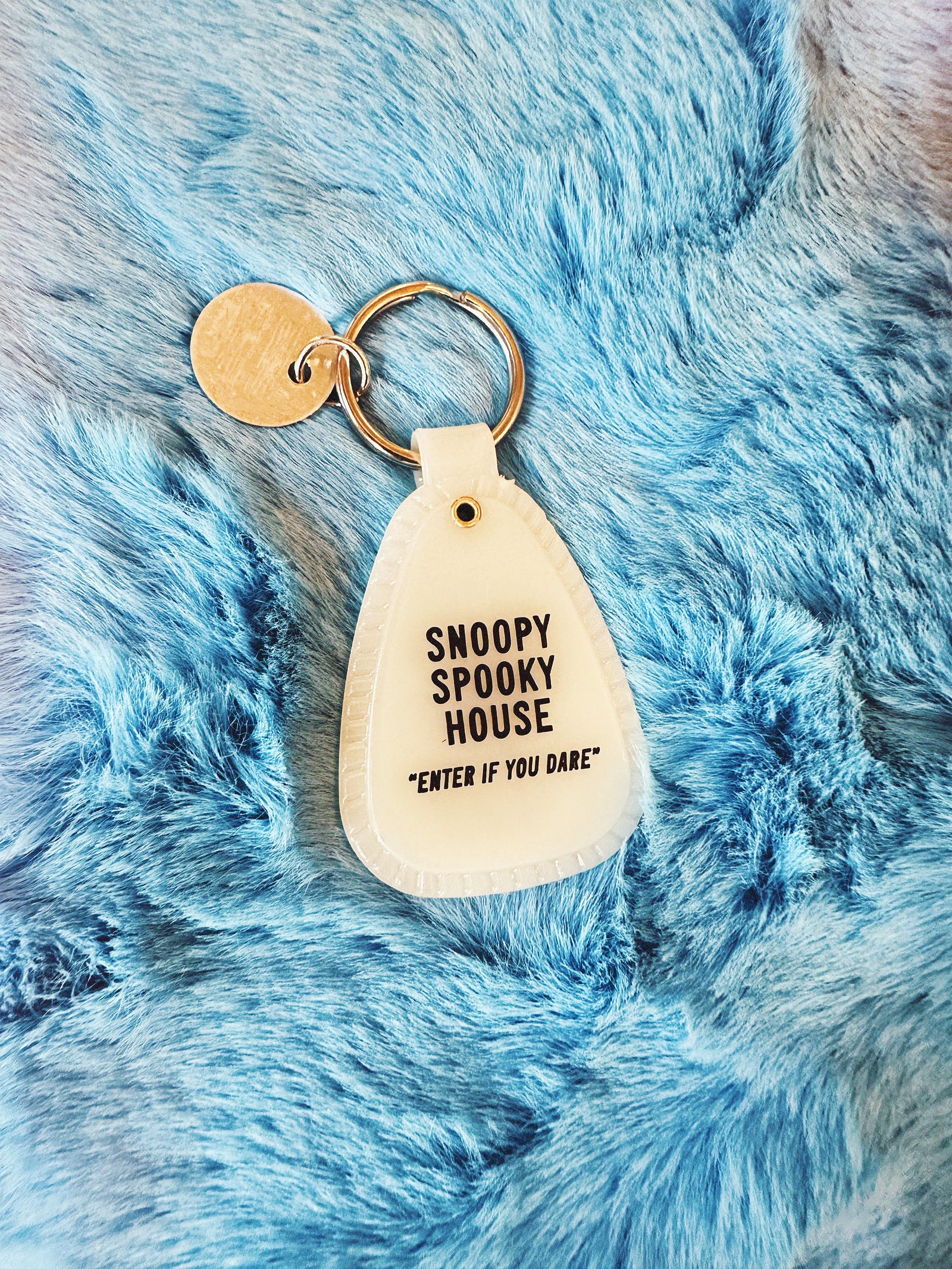 Saddle style, glow in the dark, Halloween Snoopy Mummy keychain on a fuzzy blue background. 