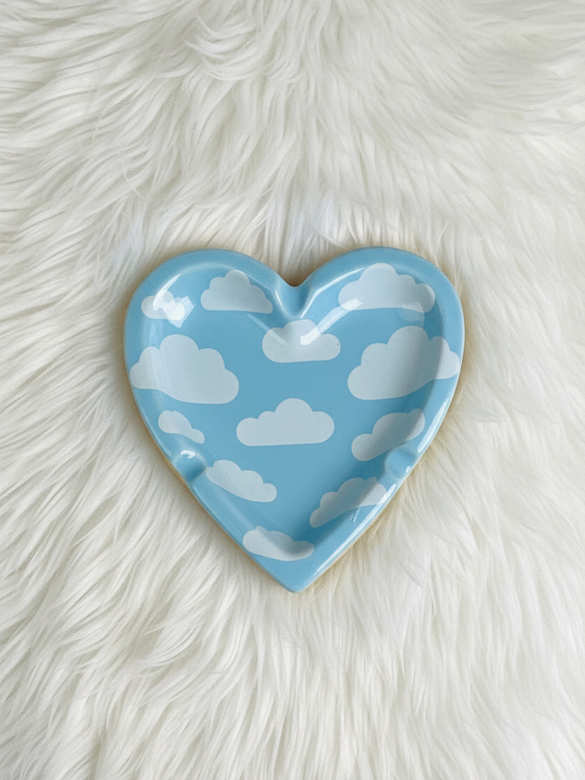 Heart-shaped blue ashtray with cloud pattern on a white fur background 