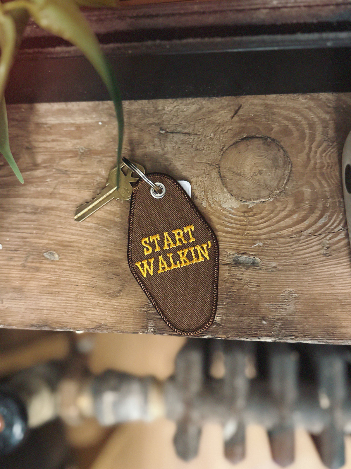 Brown embroidered keychain with 'START WALKIN' text on a wooden surface