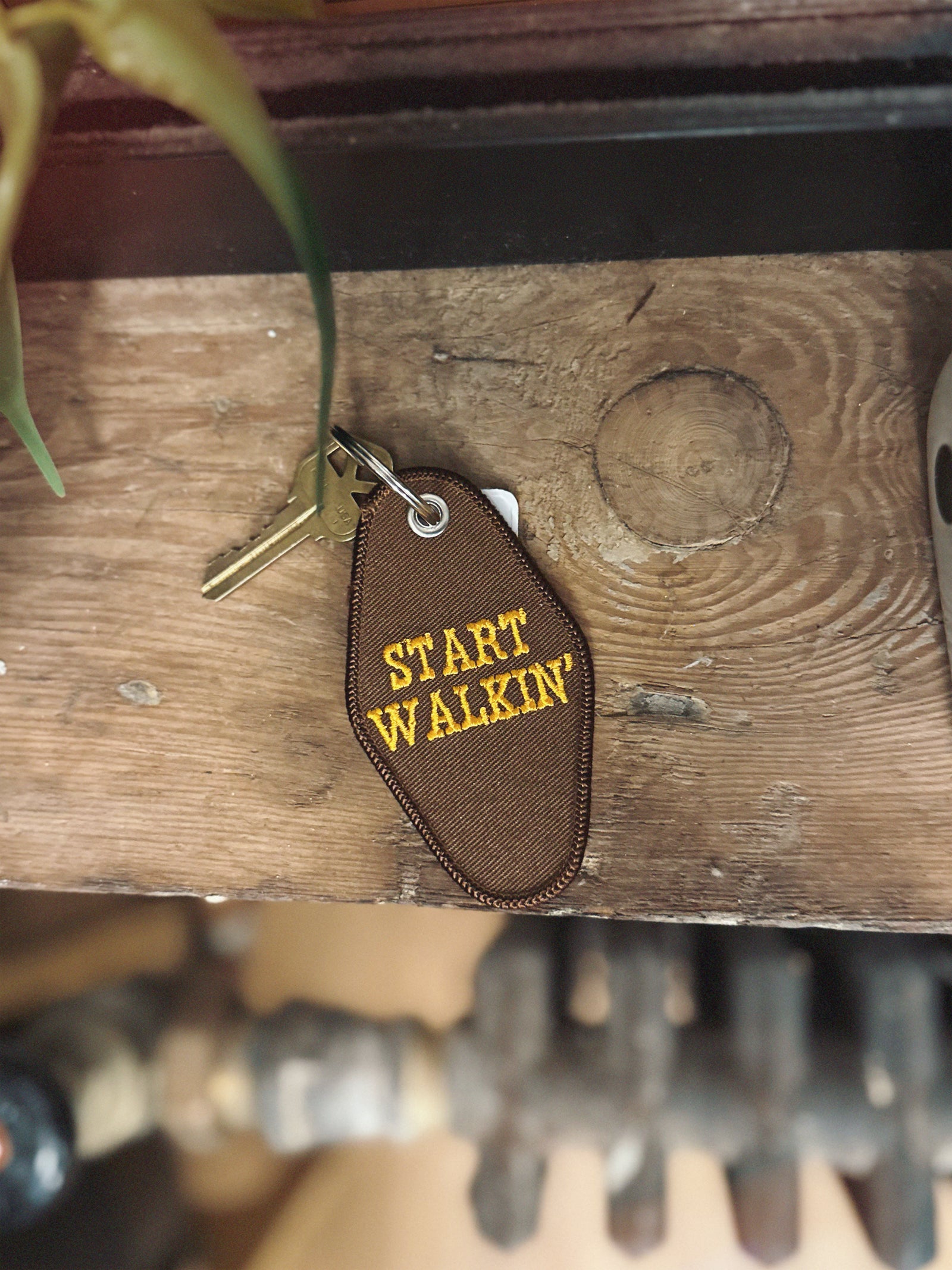 Brown embroidered keychain with 'START WALKIN' text on a wooden surface