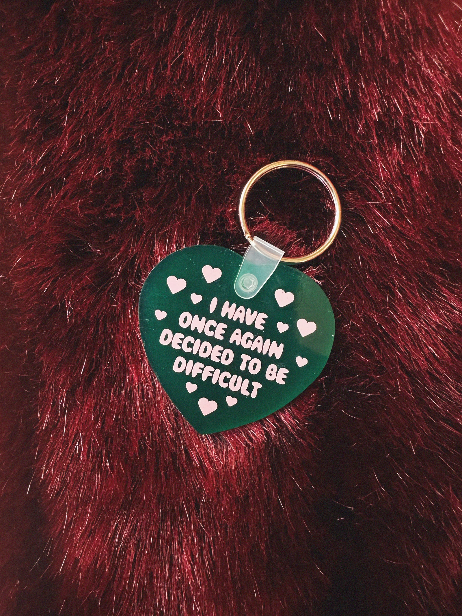 Green heart-shaped keychain with text on a red furry background