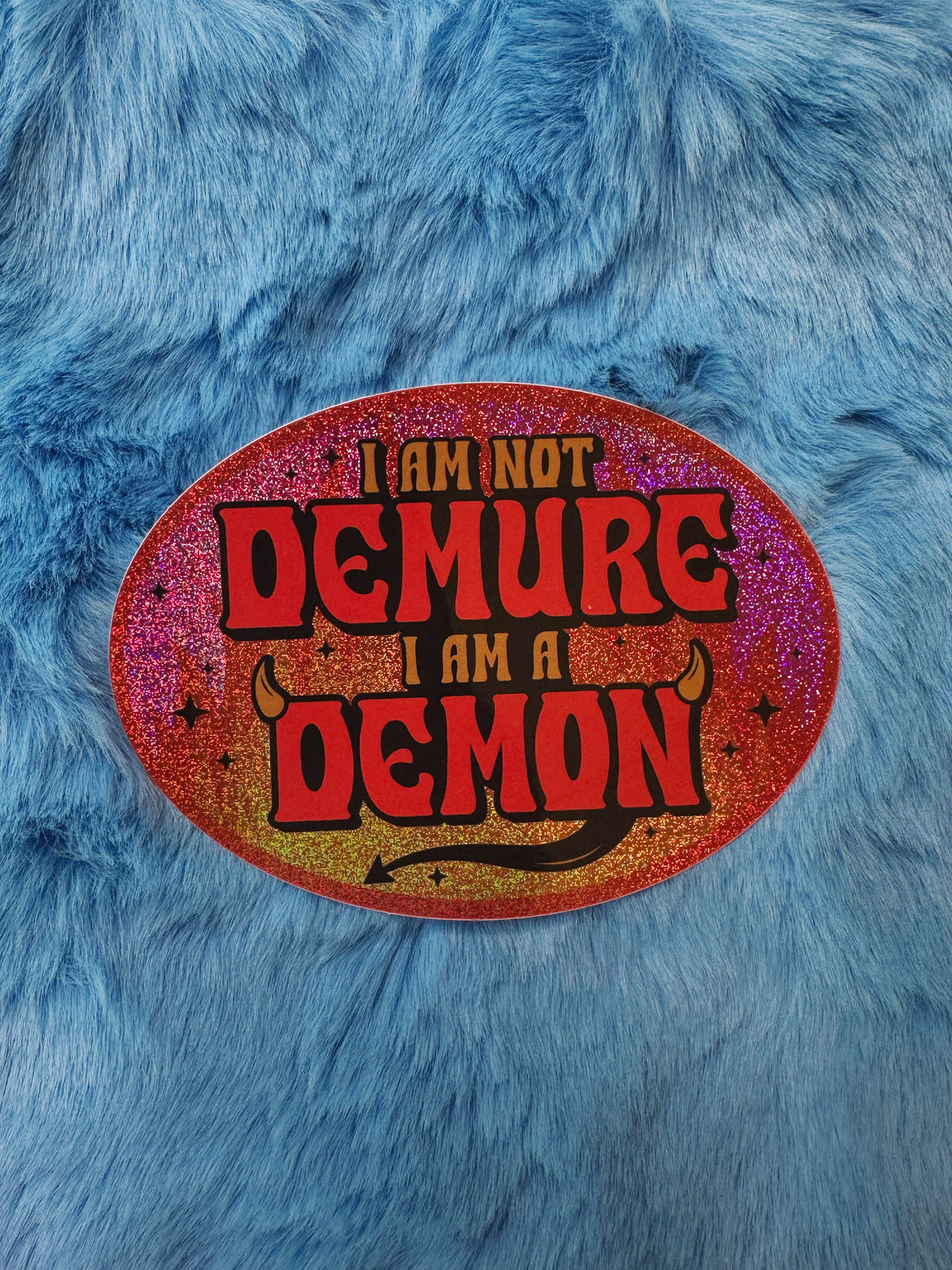 Oval sticker with &#39;I am not demure, I am a demon&#39; text on a blue furry background