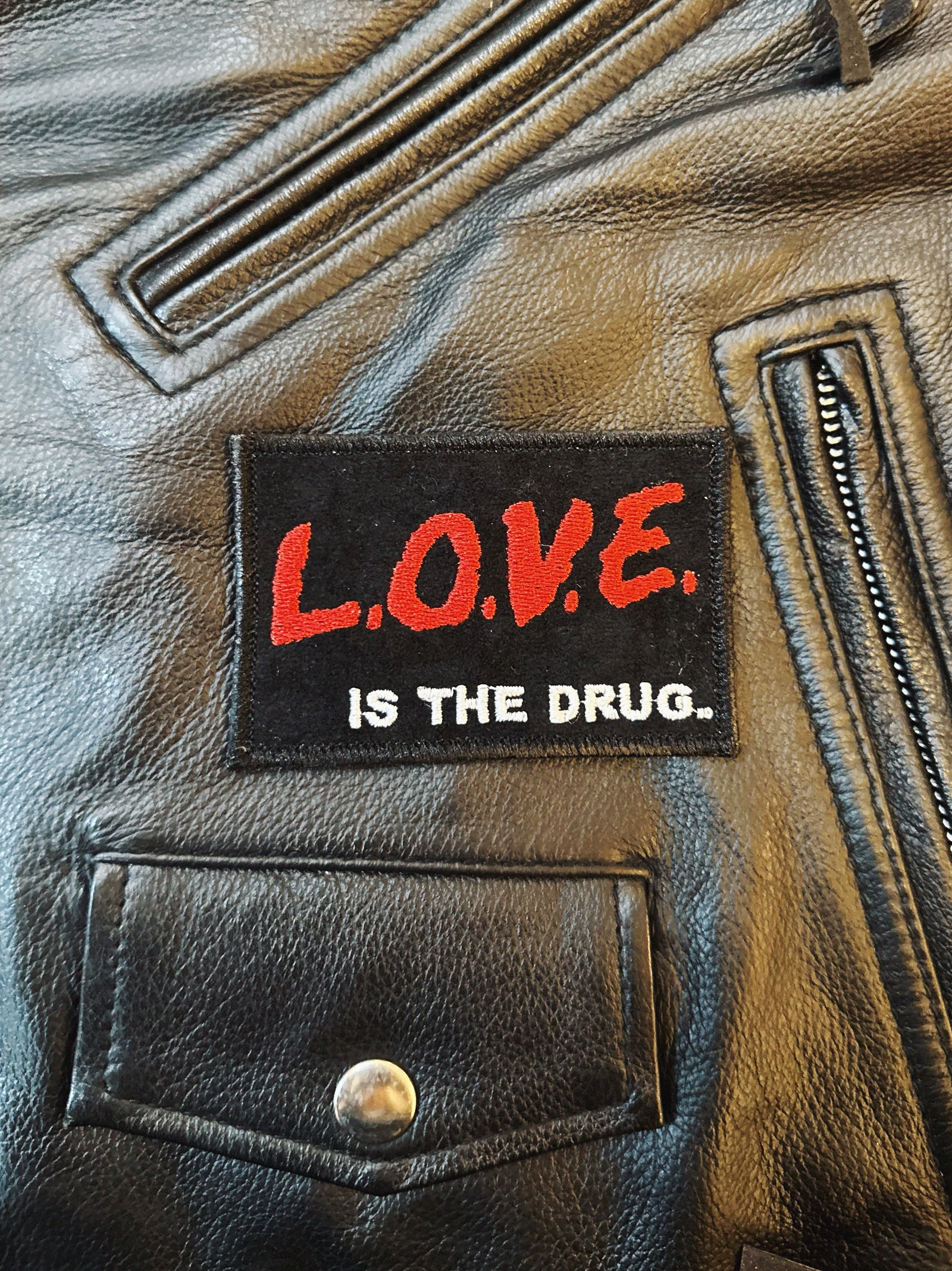 Black leather jacket with a patch reading 'L.O.V.E. IS THE DRUG.'