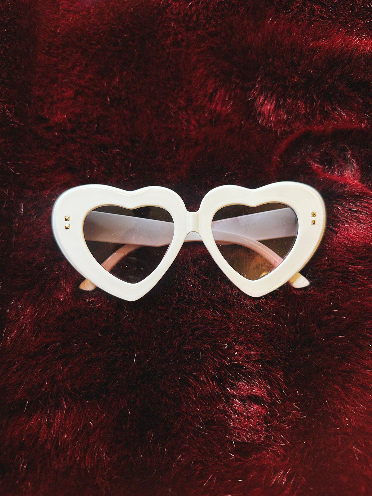 White heart-shaped sunglasses on a red fur background