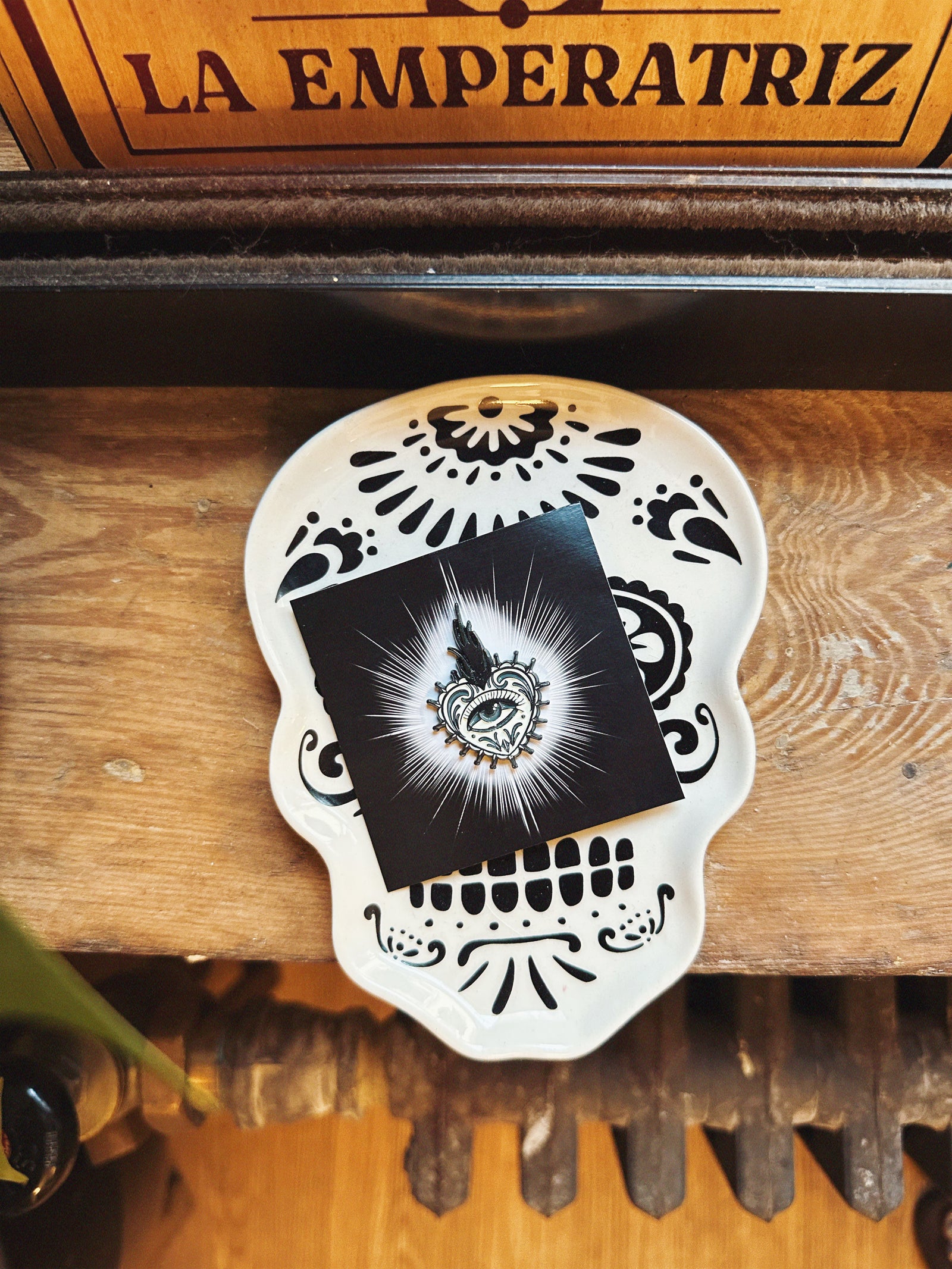 Decorative pin backing card with Sacred Heart enamel pin in black and white photographed on a black and white sugar skull tray. 