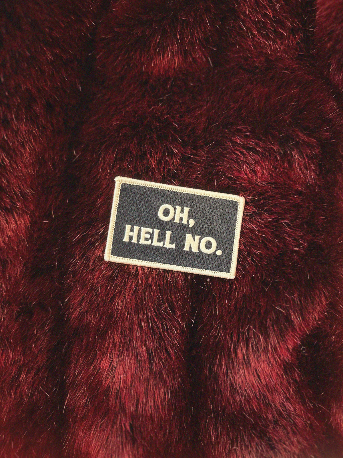 Close-up of a red textured fabric with a patch reading &#39;OH,HELL NO.&#39;