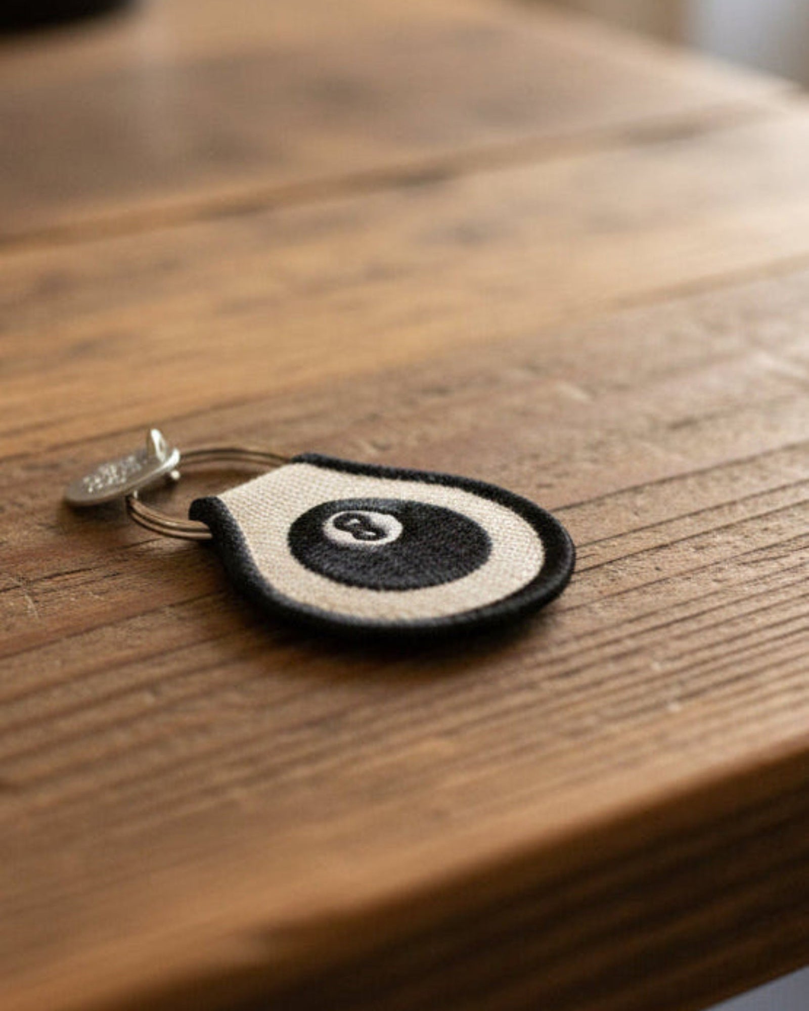 Round embroidered keychain with a black and white 8 ball design on a wooden surface
