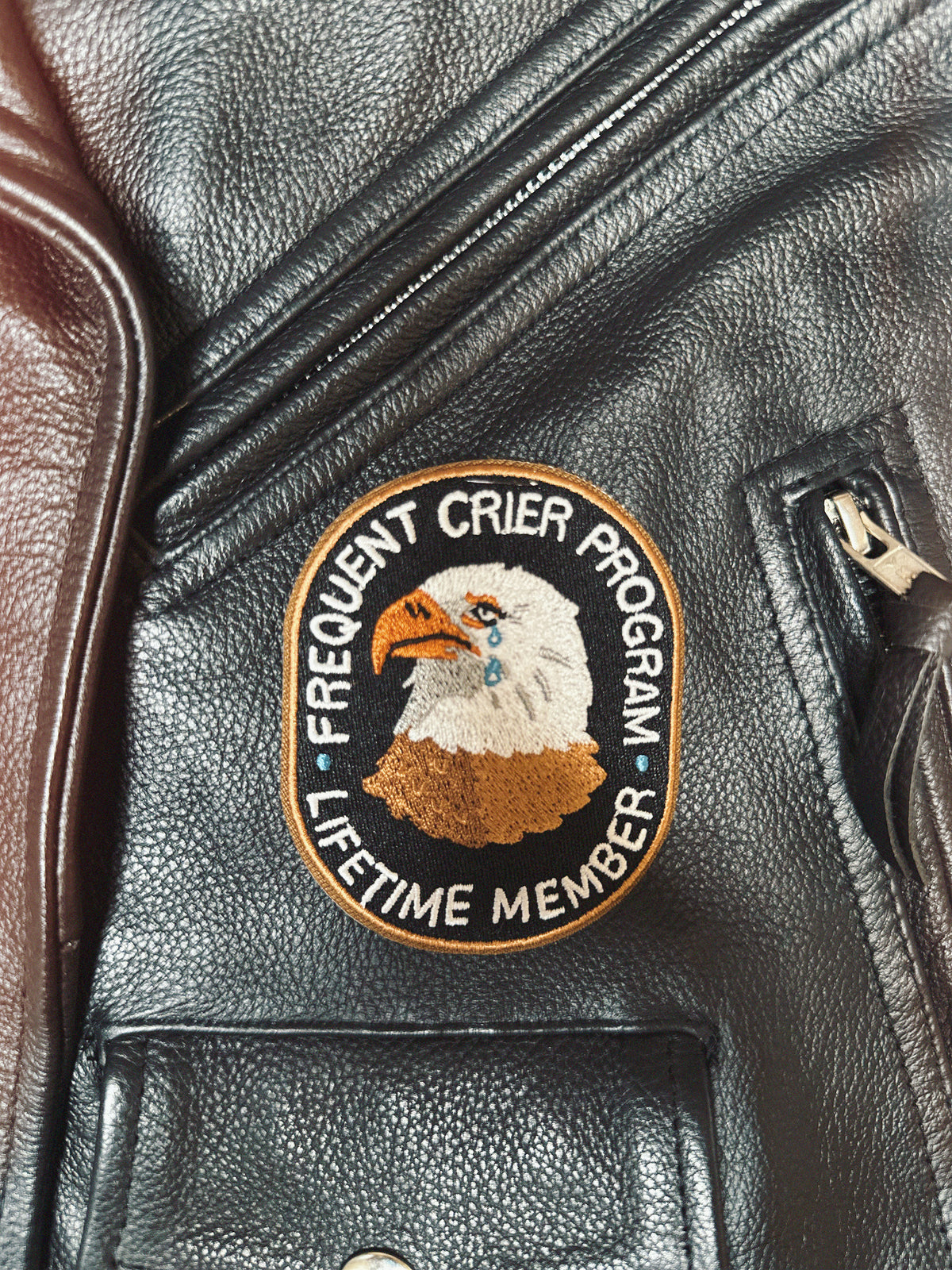 Frequent Crier Program black and gold patch on a leather jacket with an eagle design and text.