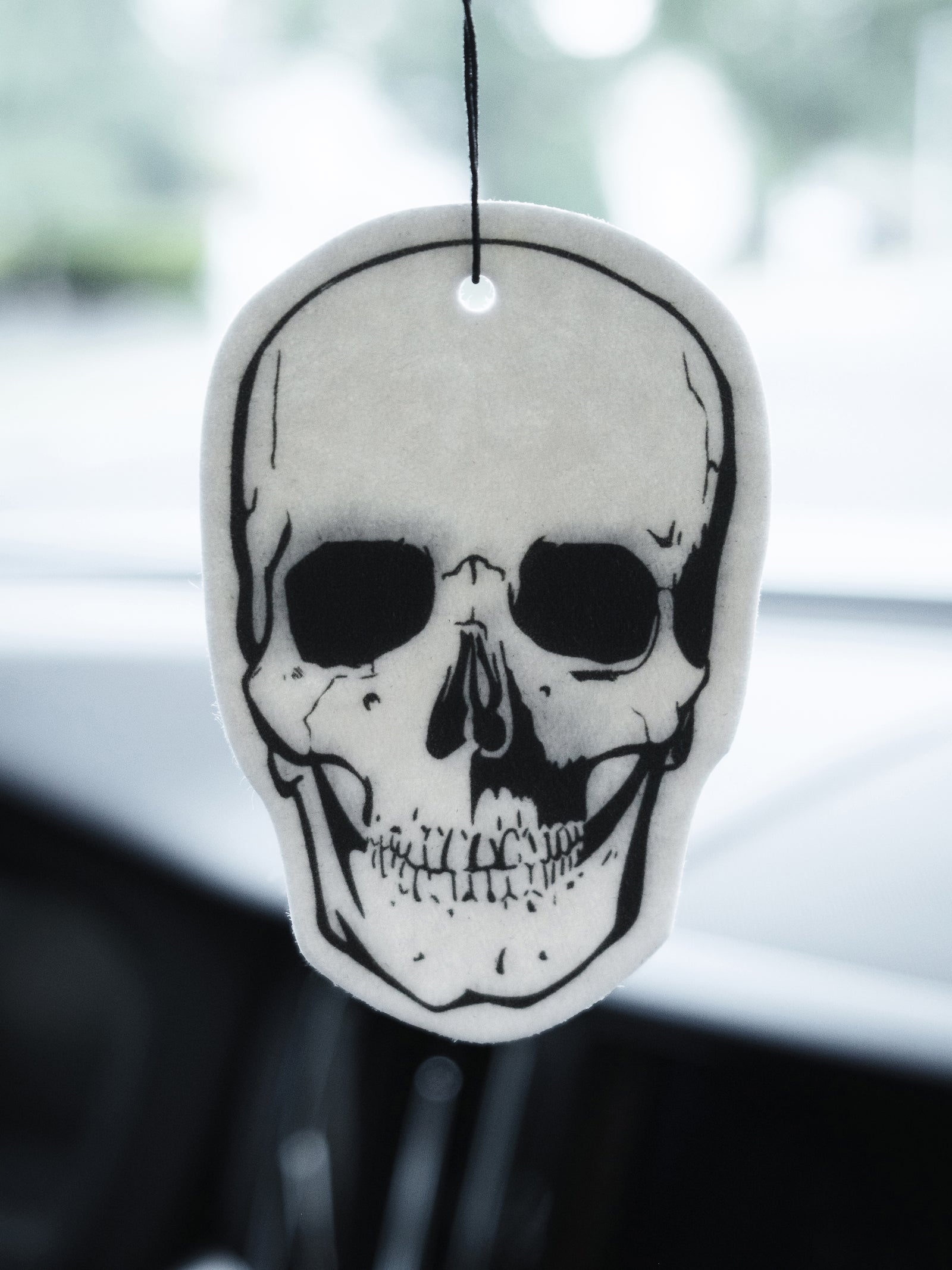 A skull-shaped air freshener hanging from a rearview mirror, predominantly white with black detailing.