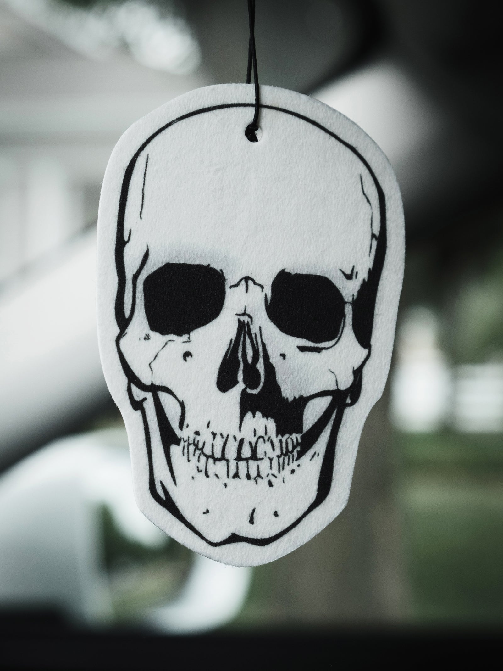 A skull-shaped air freshener hanging from a rearview mirror, predominantly white with black detailing.