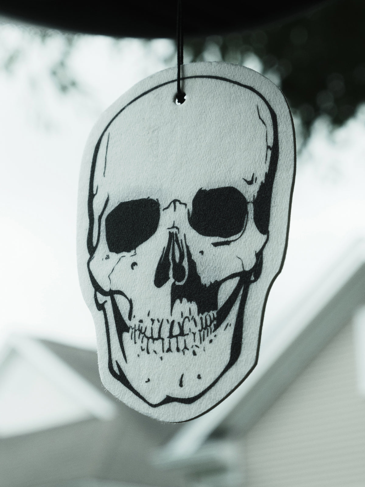 A skull-shaped air freshener hanging from a rearview mirror, predominantly white with black detailing.