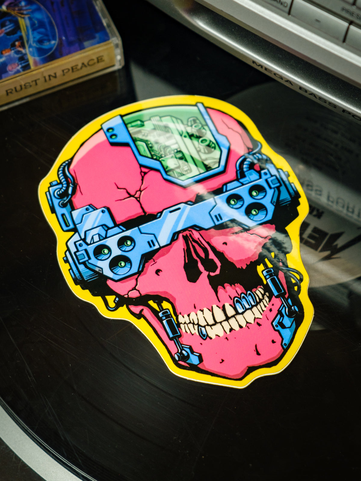 A colorful vinyl sticker depicting a skull with cyber punk aesthetics, including blue and yellow electronic components over a pink and red background.