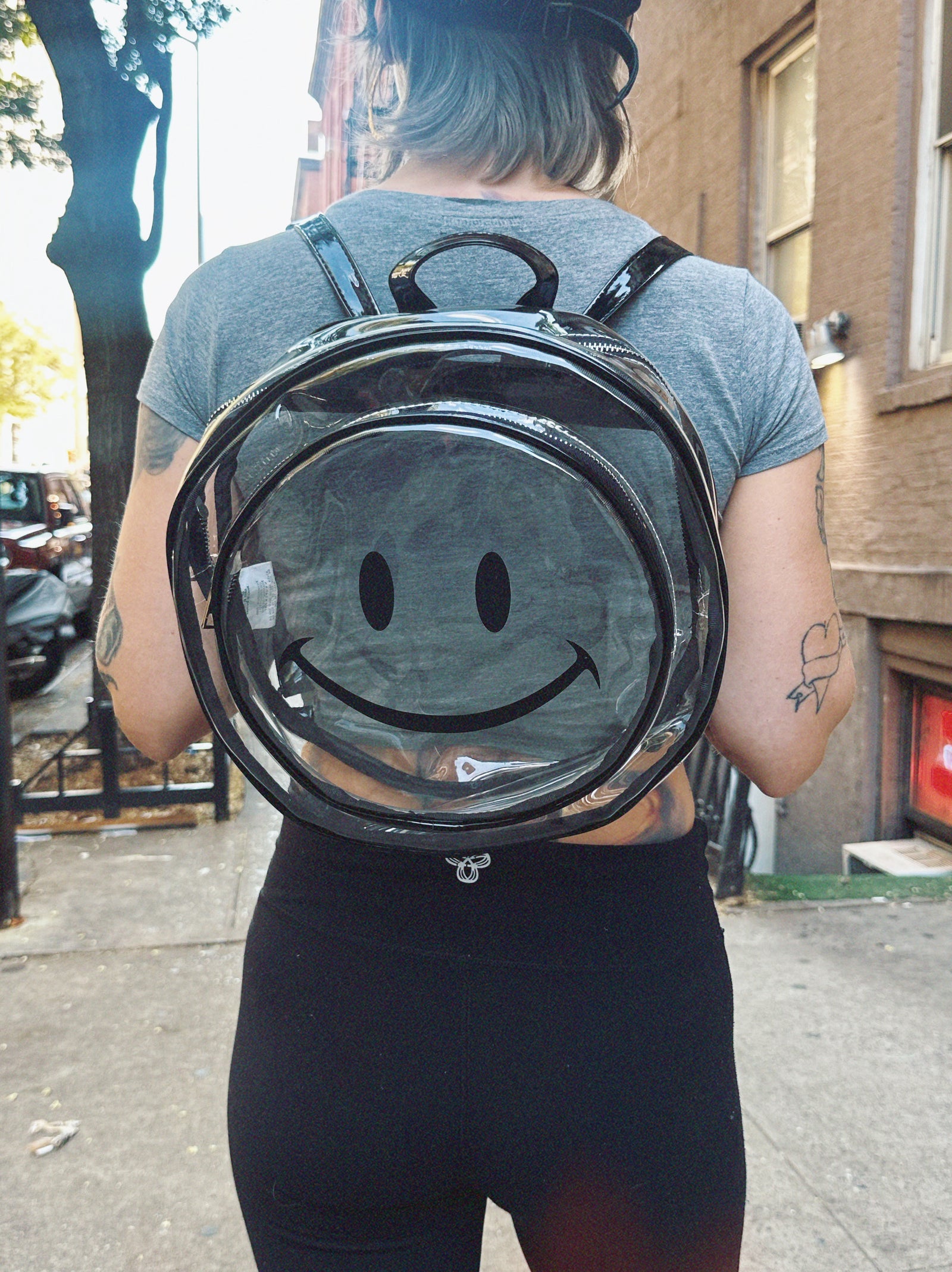 Person wearing a transparent backpack with a smiley face design outdoors.