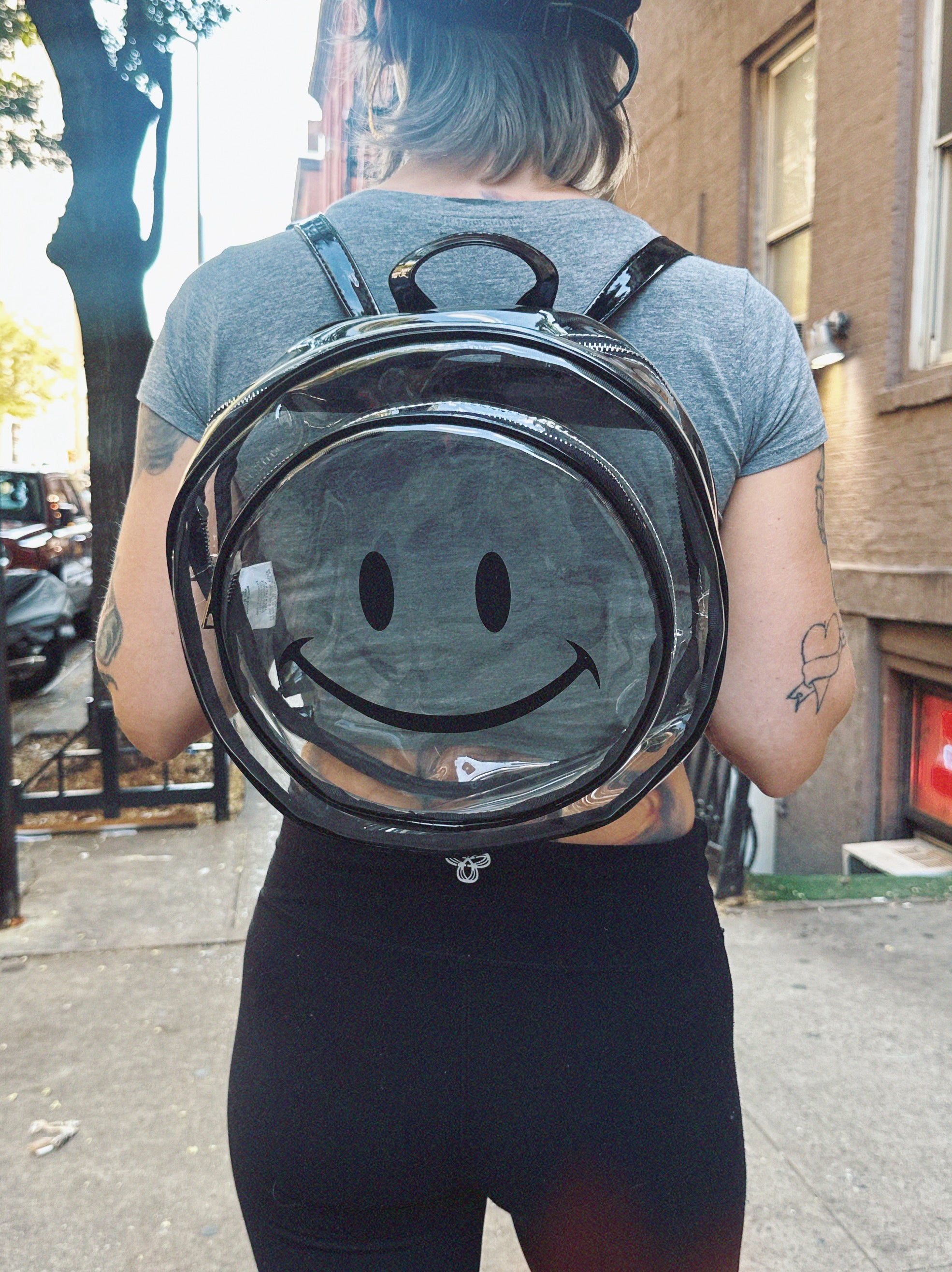 Person wearing a transparent backpack with a smiley face design outdoors.