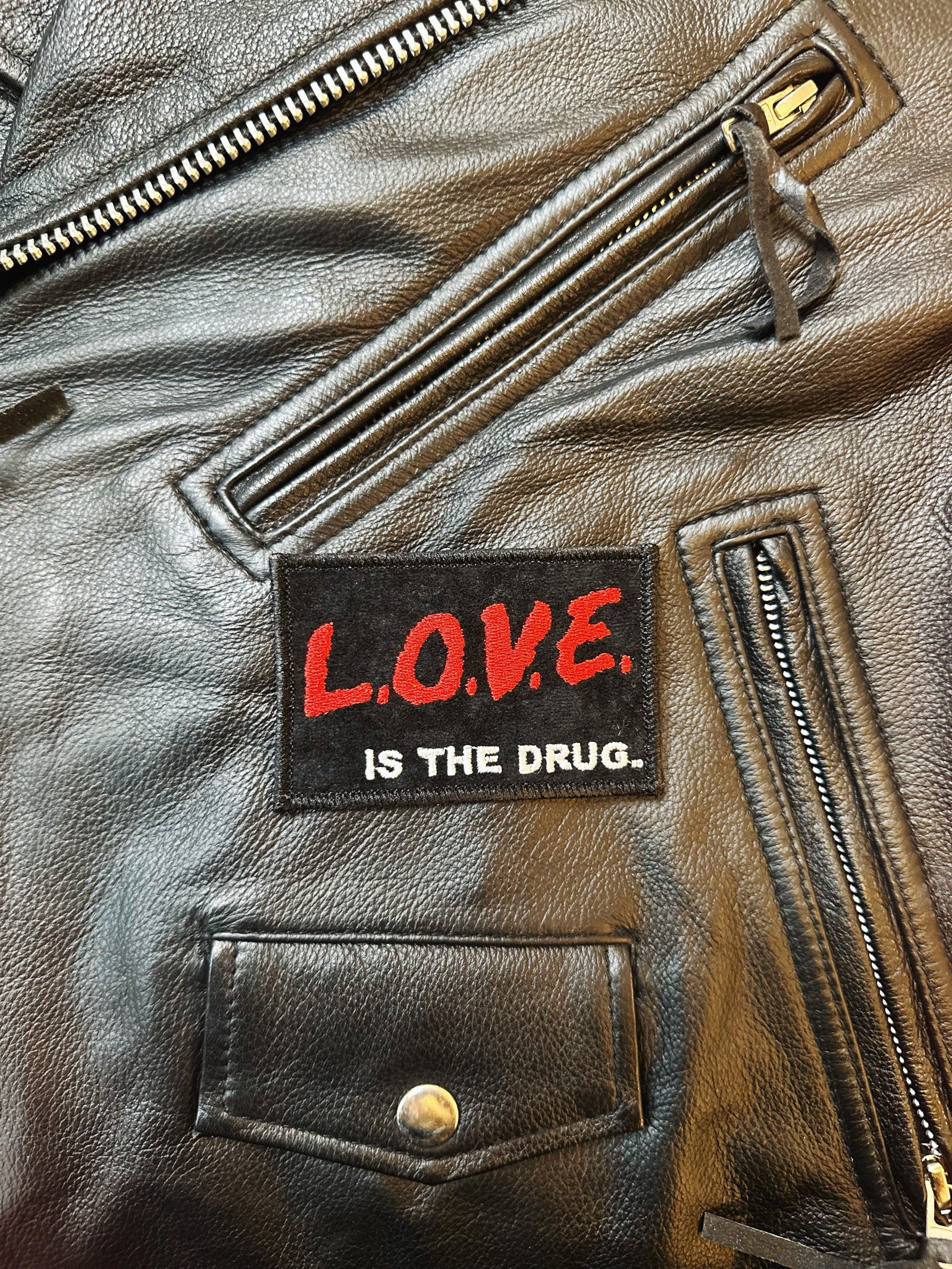 Black leather jacket with a patch reading 'L.O.V.E. IS THE DRUG.'