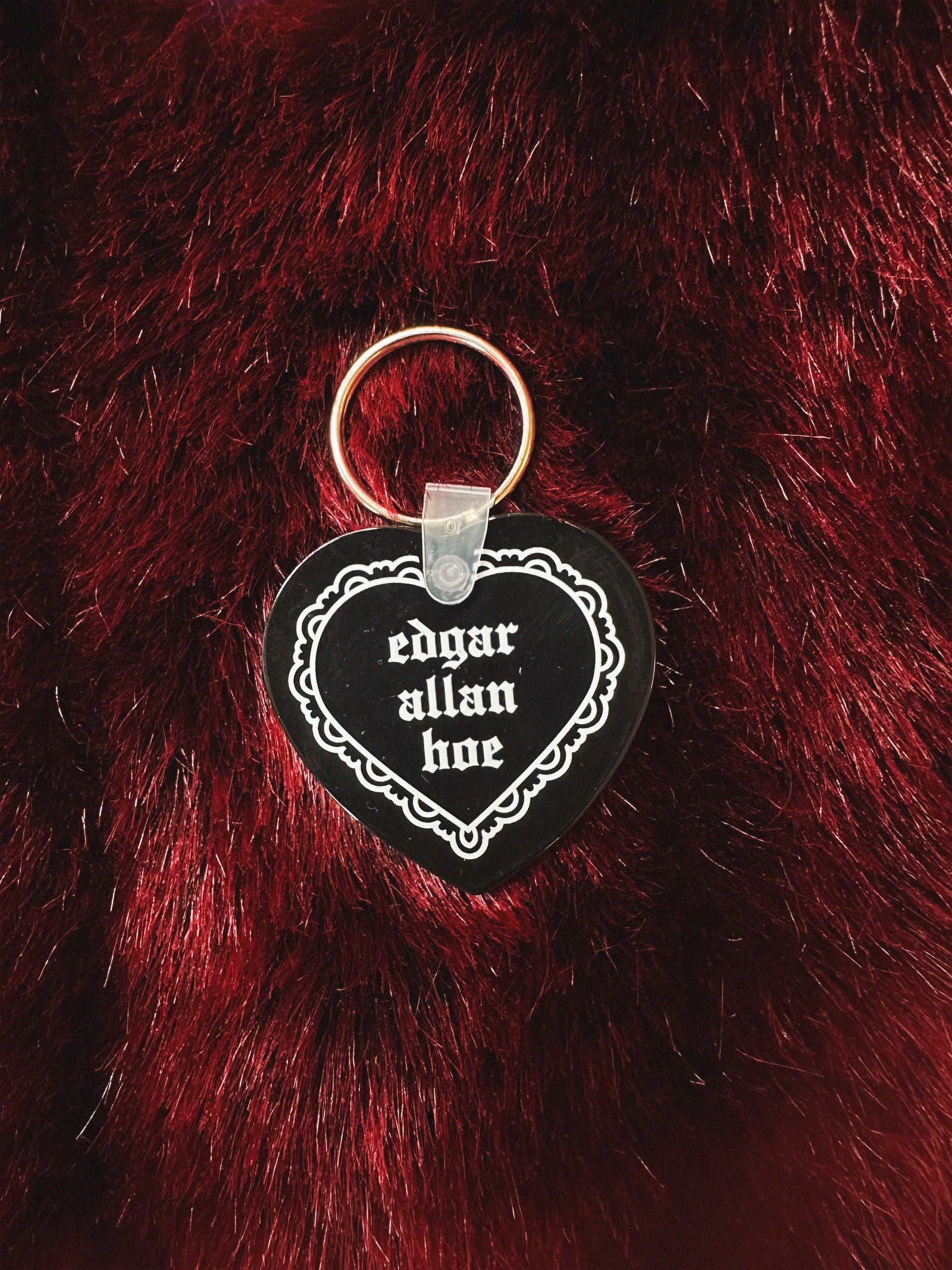 Heart-shaped keychain with 'edgar allan hoe' text on a red furry background