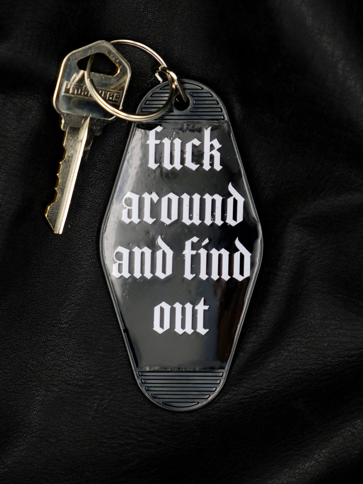 black motel style keychain with a key for size and use reads Fuck Around and Find Out in an old english type font in white. 