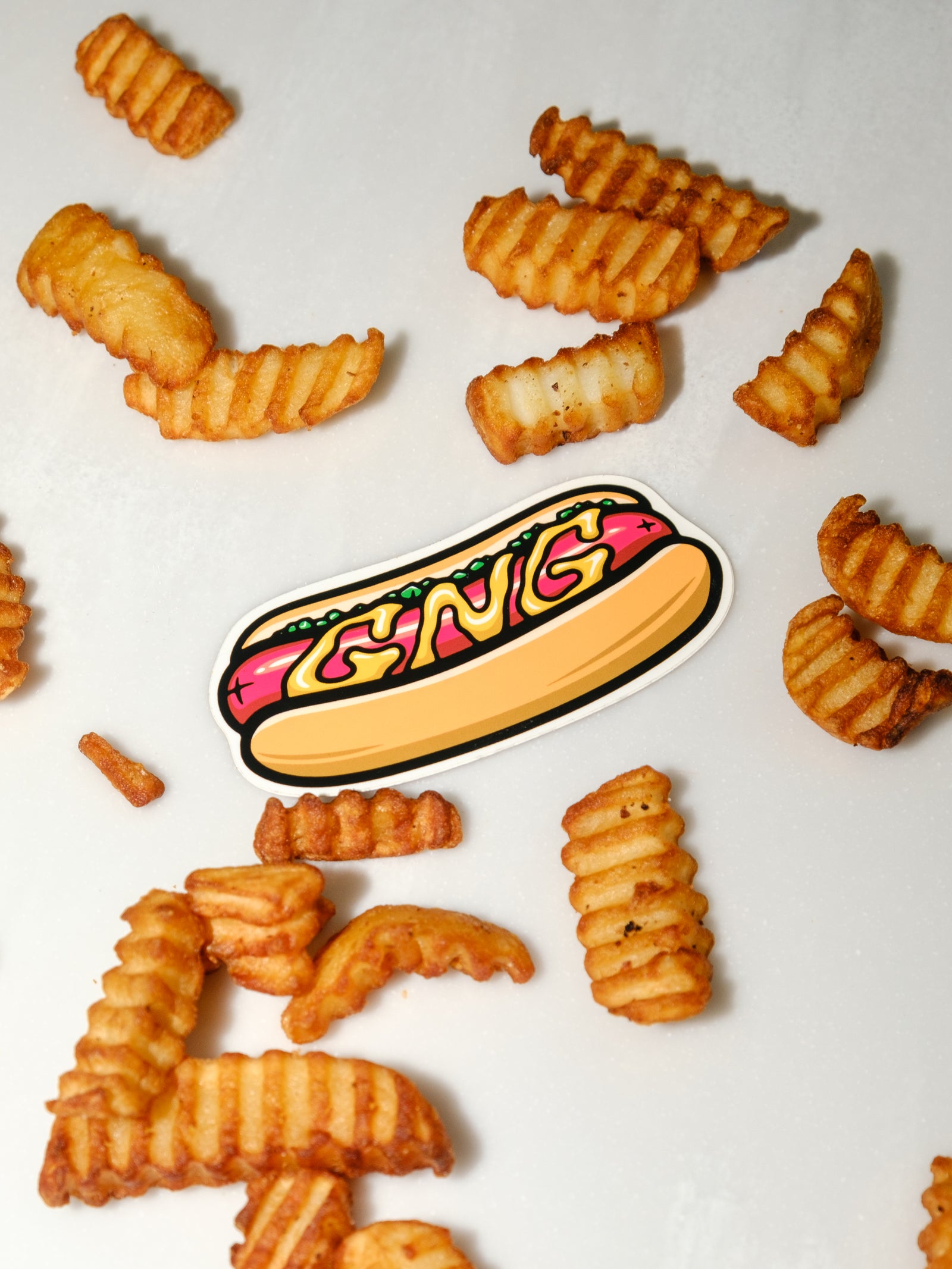 A vinyl sticker with a hot dog design, labeled 'GNG', placed on a table with fries and ketchup.