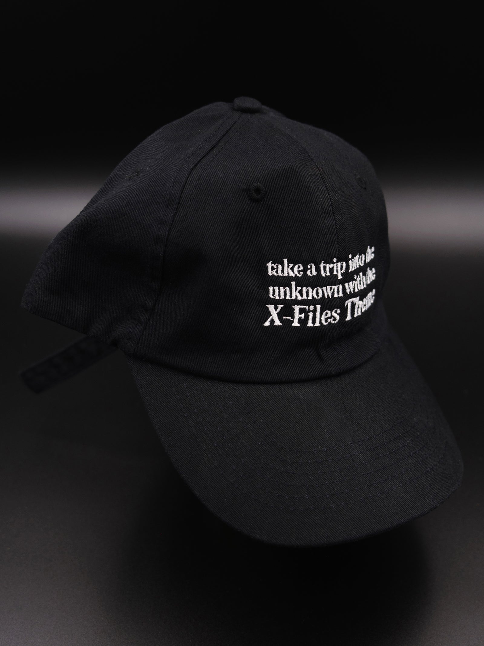 black hat with white embroidered text reads "take a trip into the unknown with the X-Files theme"