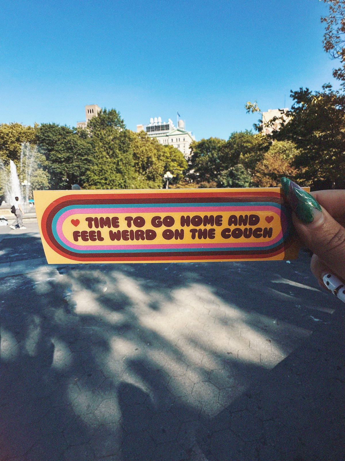 colorful sticker photographed in washington square park nyc. sticker reads &quot;time to go home and feel weird on the couch&quot;