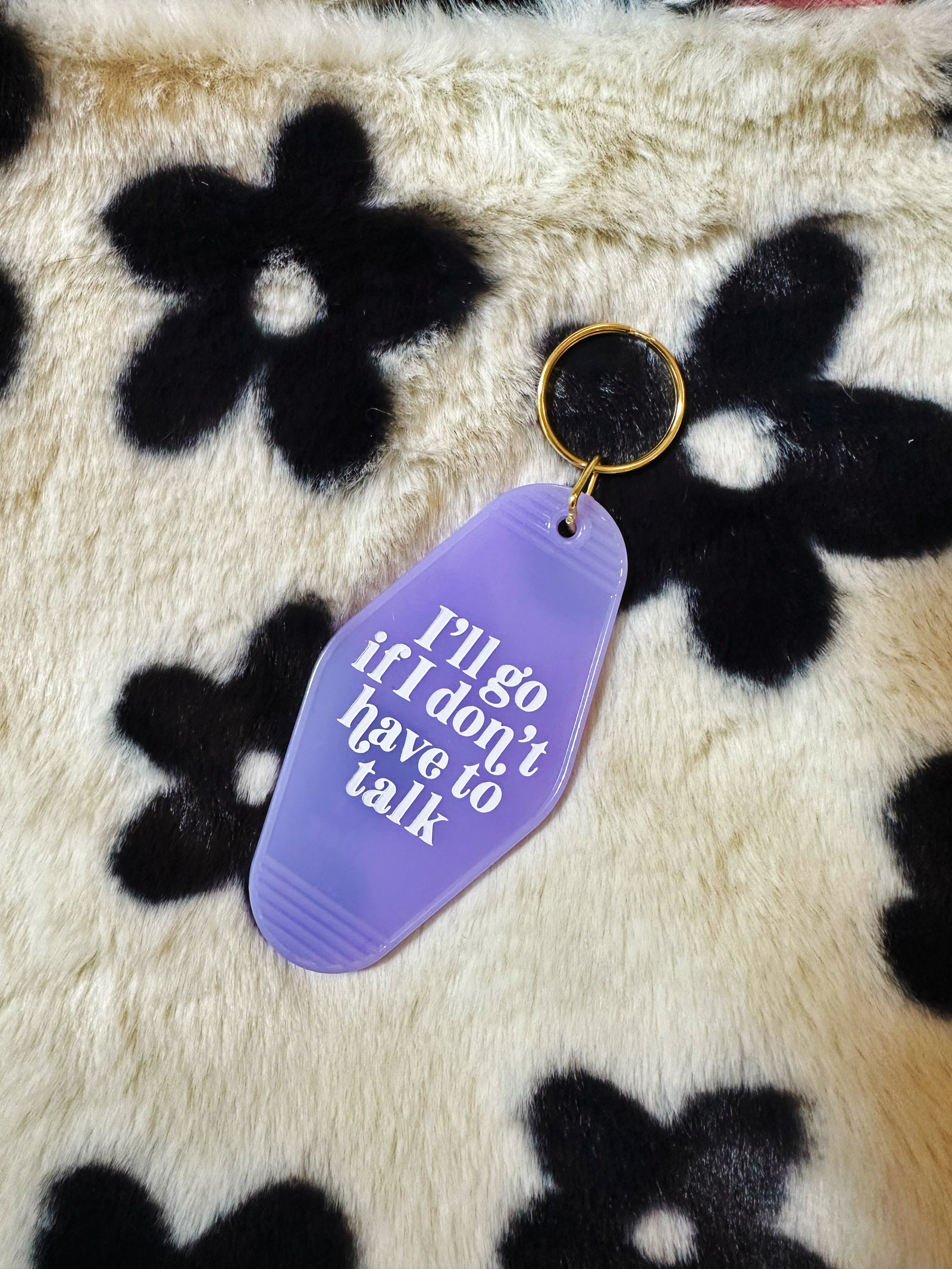 Purple keychain tag with text on a floral-patterned fabric background. Text reads "I'll go if I don't have to talk"