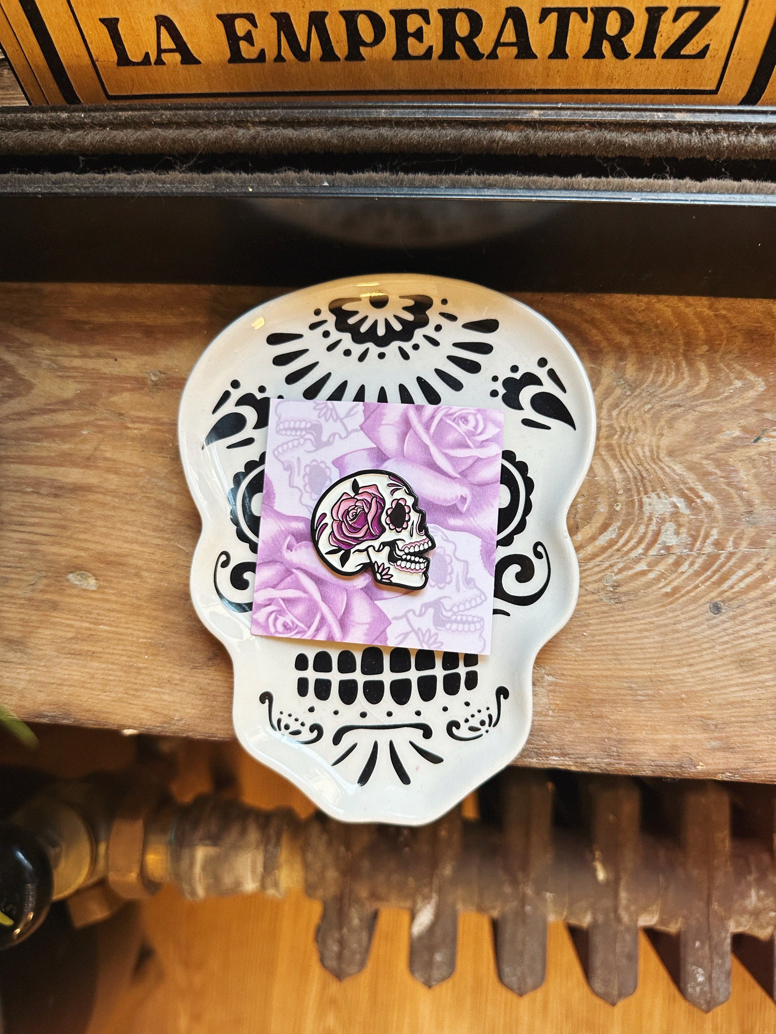 Decorative skull with a pink card featuring a skull and rose design on a wooden surface.