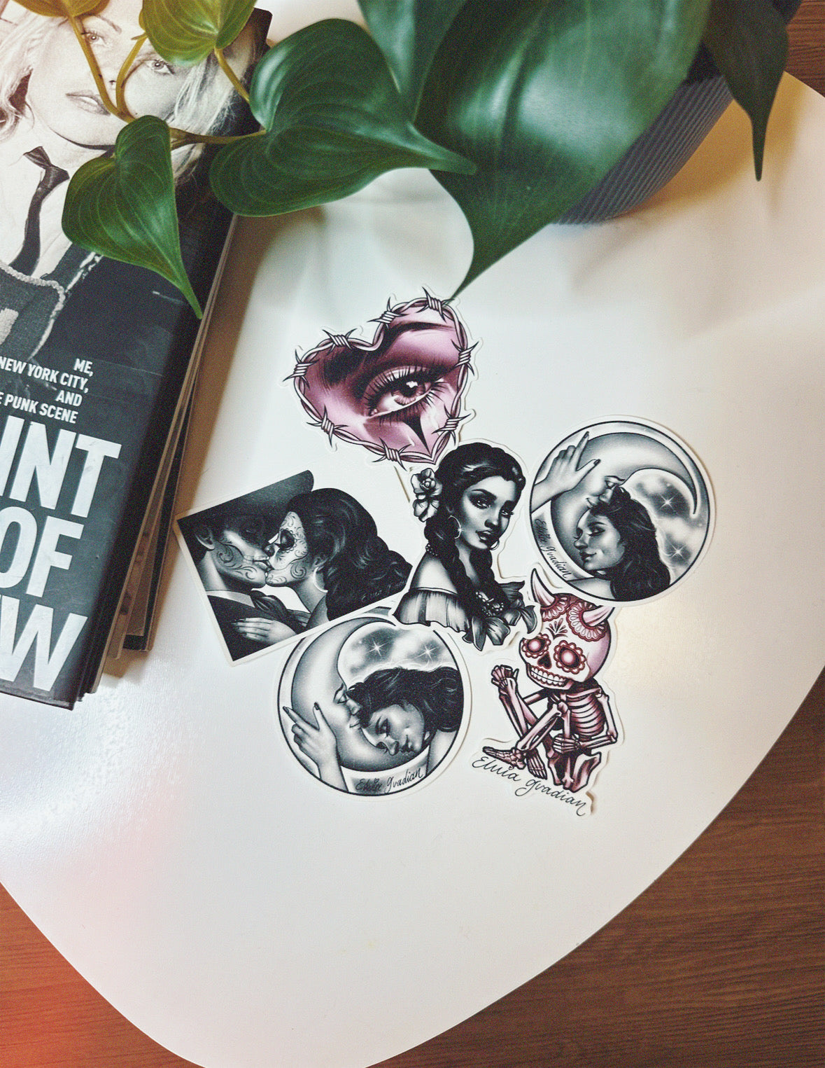 Set of sticker designs on a white table with a book and green leaves in the background