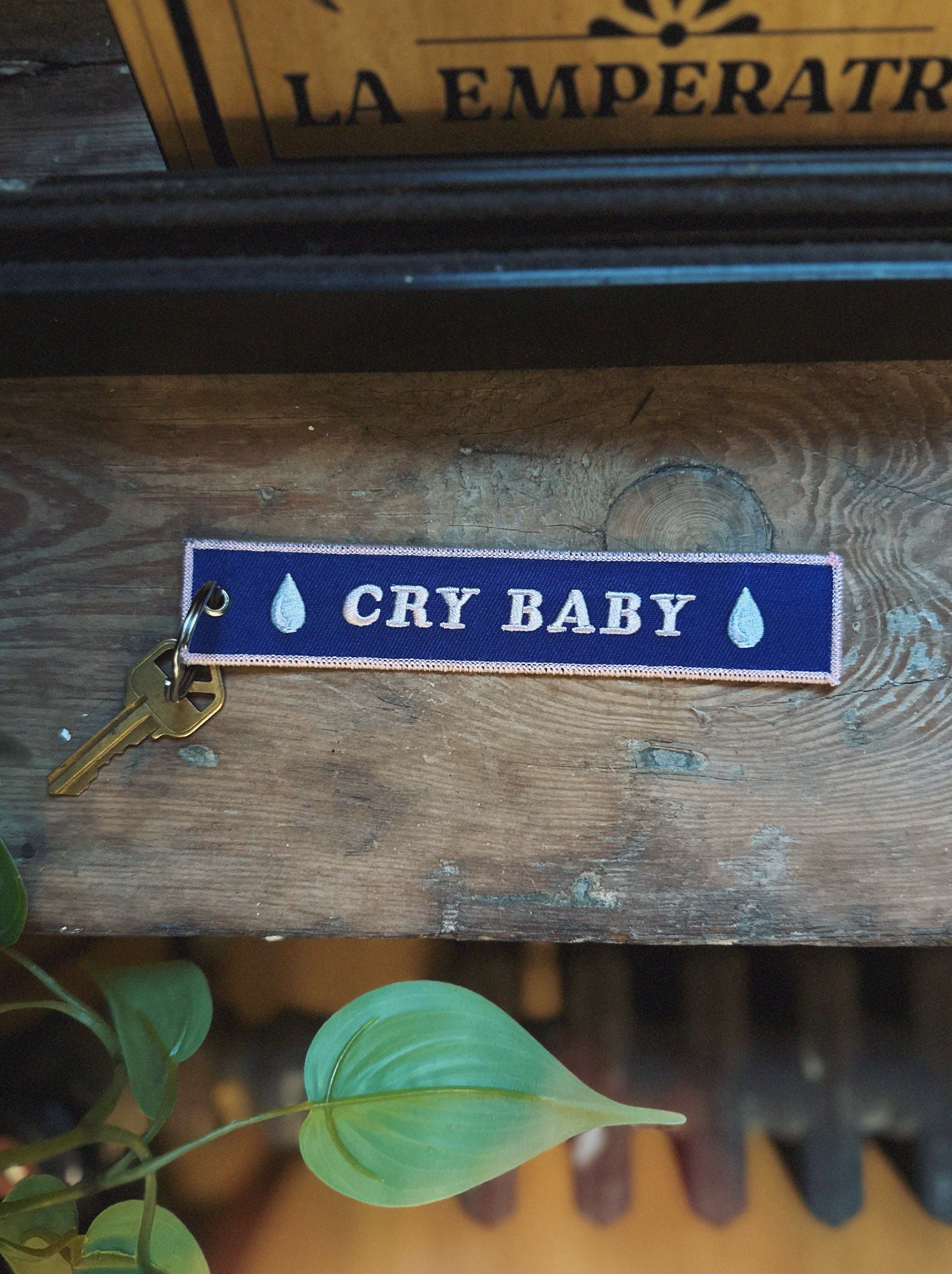 Embroidered blue keychain with 'CRY BABY' text on a wooden surface