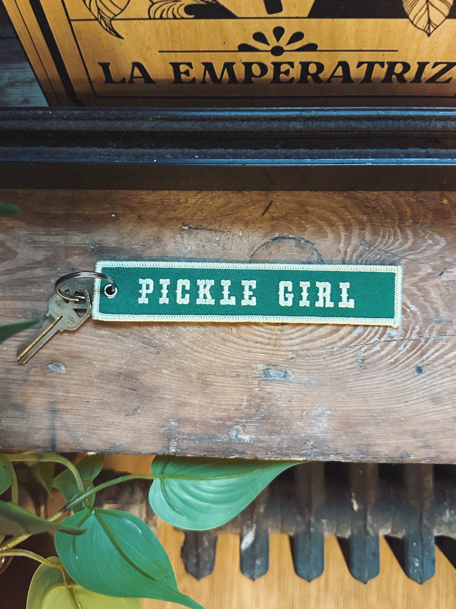 Green embroidered keychain with 'Pickle Girl' text on a wooden surface