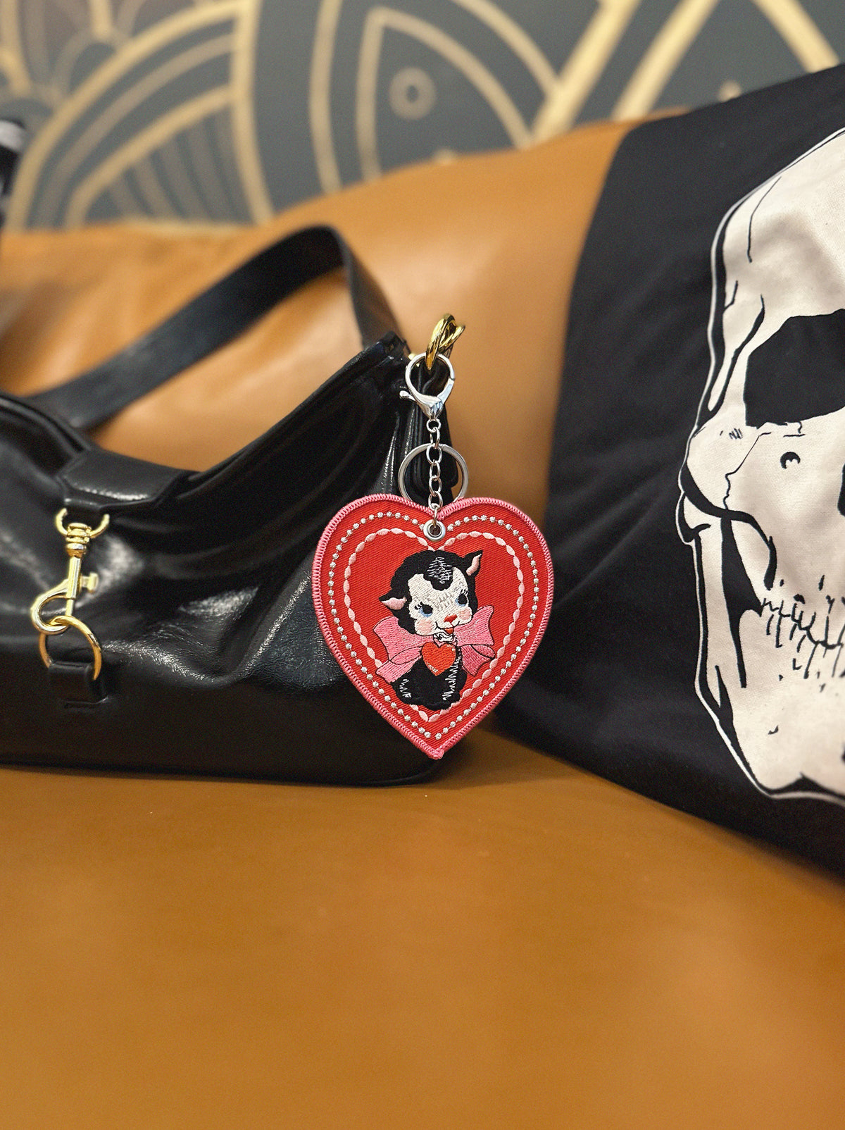 Heart-shaped keychain with cartoon sheep character attached to a black handbag on a brown surface.