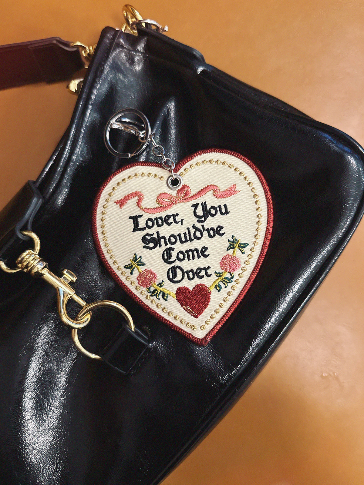 Heart-shaped off white keychain/bag charm with text on a black leather bag