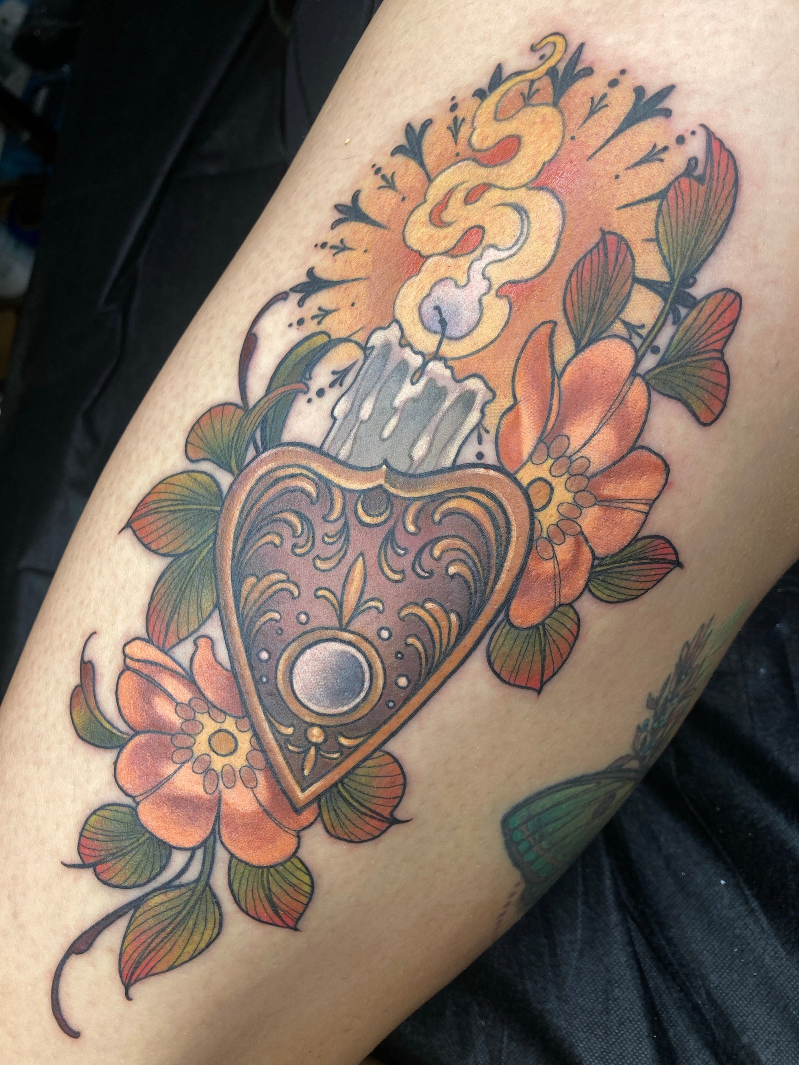 Neo traditional, color Planchette and candle tattoo by Charlotte Timmons. This Fall colored tattoo features an ornate halo, orange flowers and green leaves. 