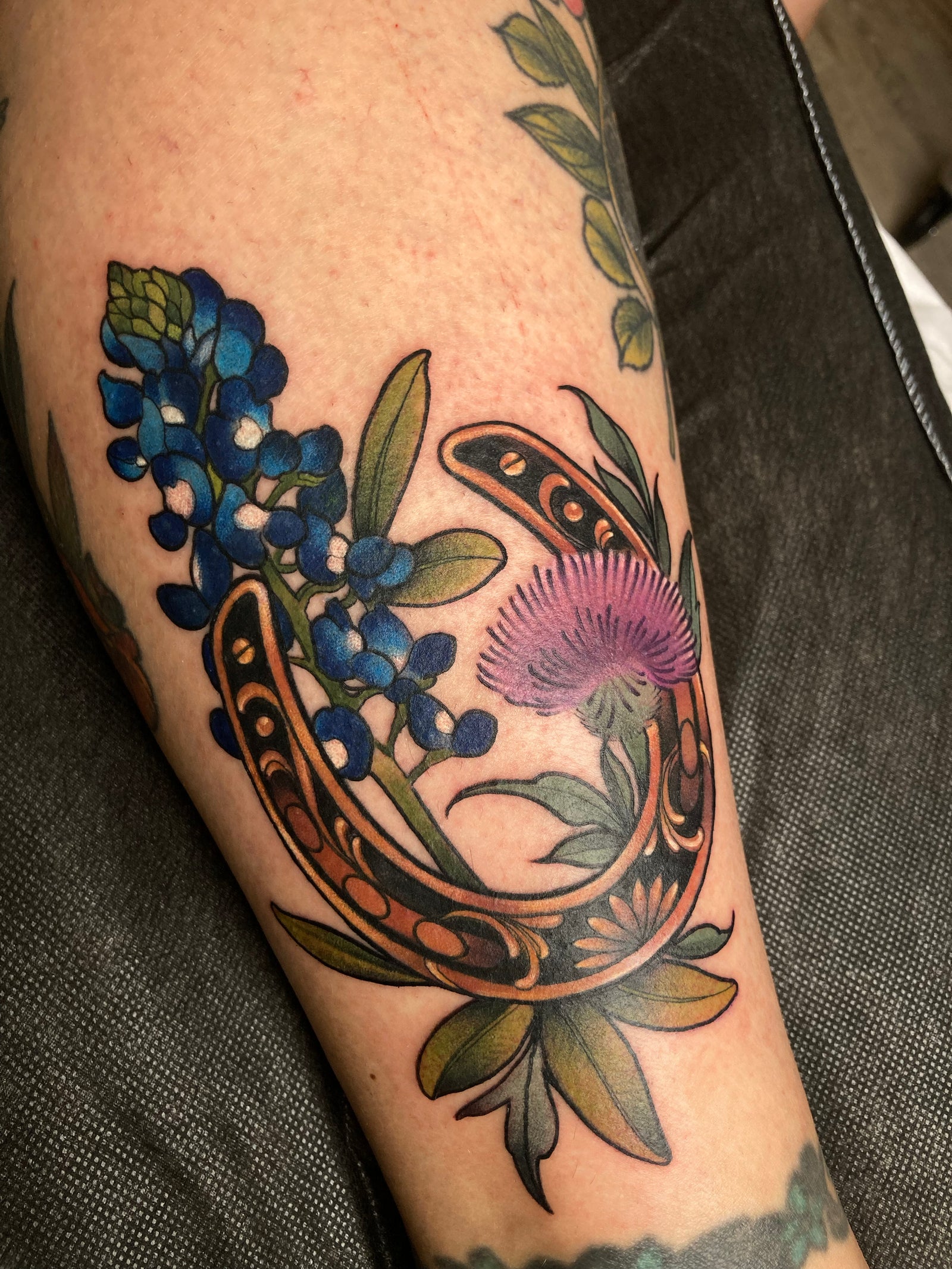 Neo traditional gold and black horseshoe tattoo by Charlotte Timmons featuring a lupine bluebonnet and Texas thistle.