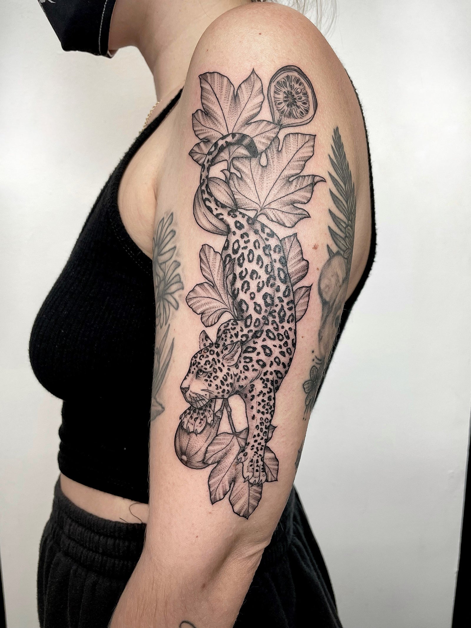 Black and gray, delicate, fineline Leopard and botanical upper arm tattoo by Janice Danger