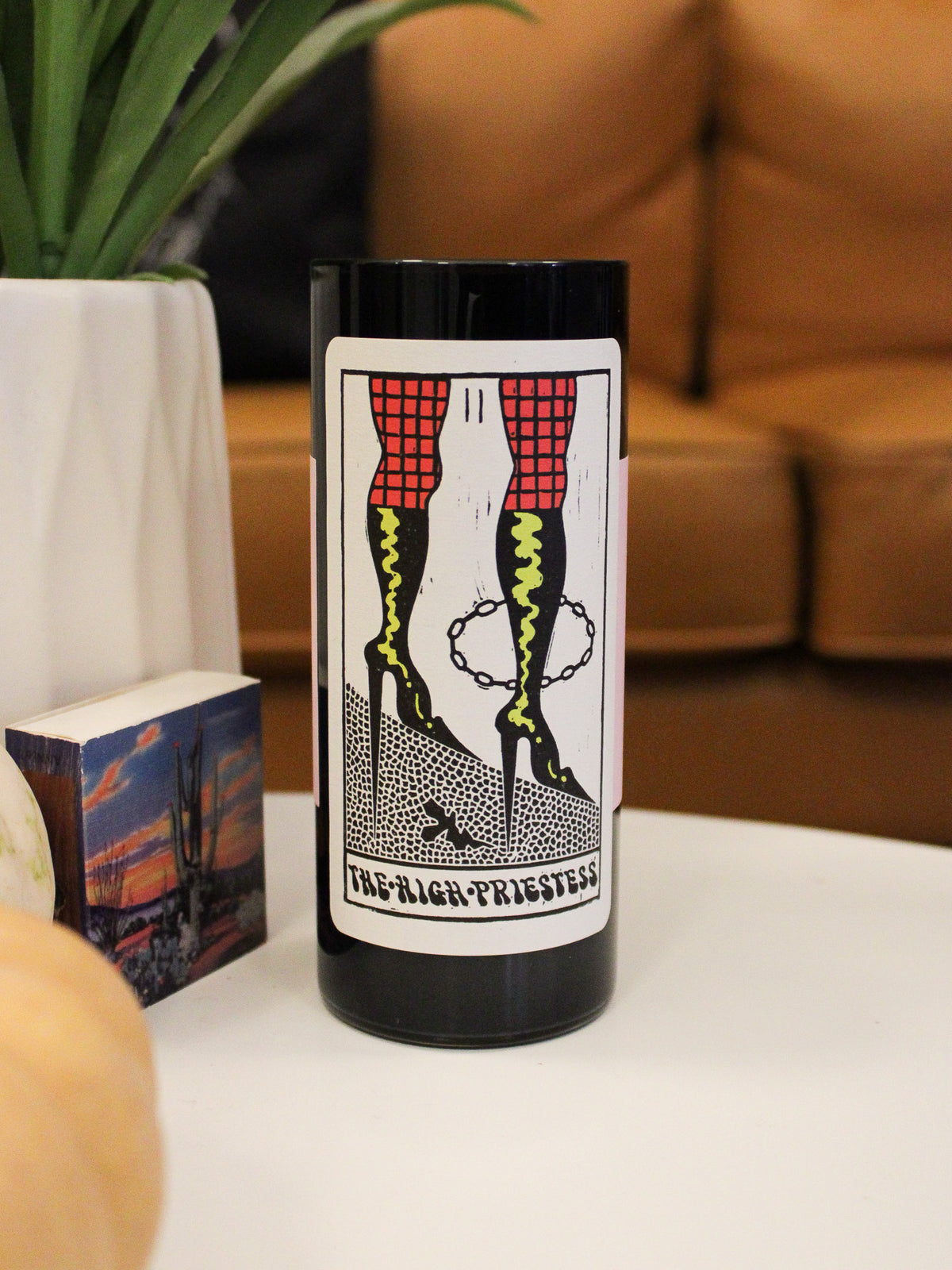 black glass tall votive candle with tarot card style label reading &quot;The High Priestess&quot;. Features an illustration of stiletto boots. 