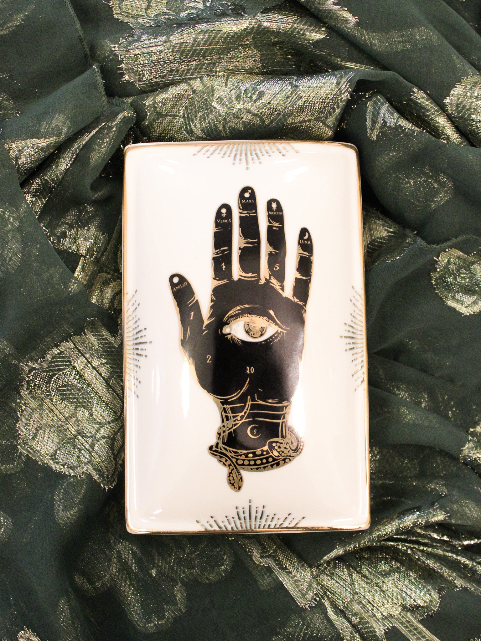 ceramic trinket box with black and gold hand graphic and details. Photographed on a green and gold background