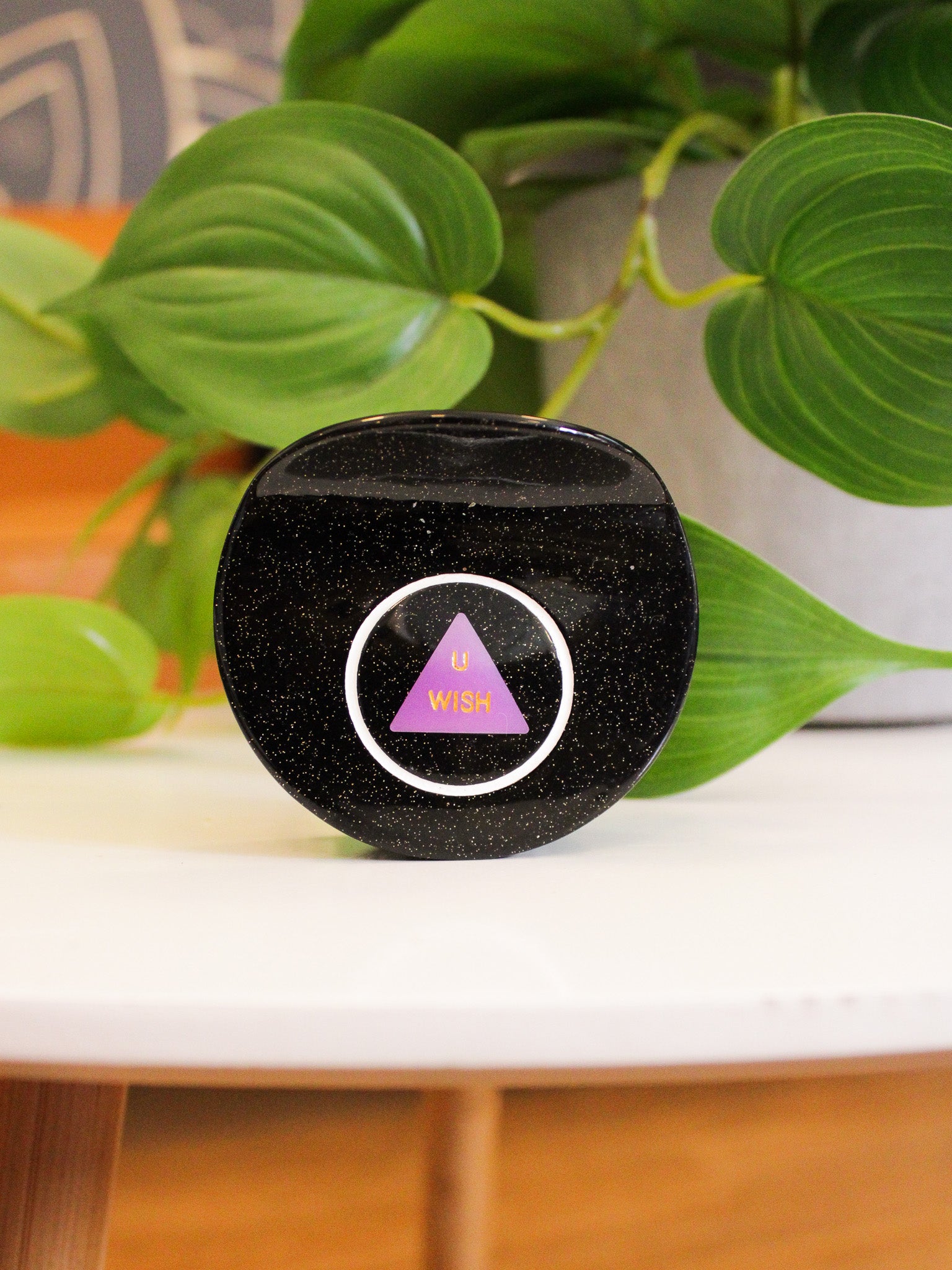 Black spherical object with a purple triangle and white circle on a surface with green leaves in the background